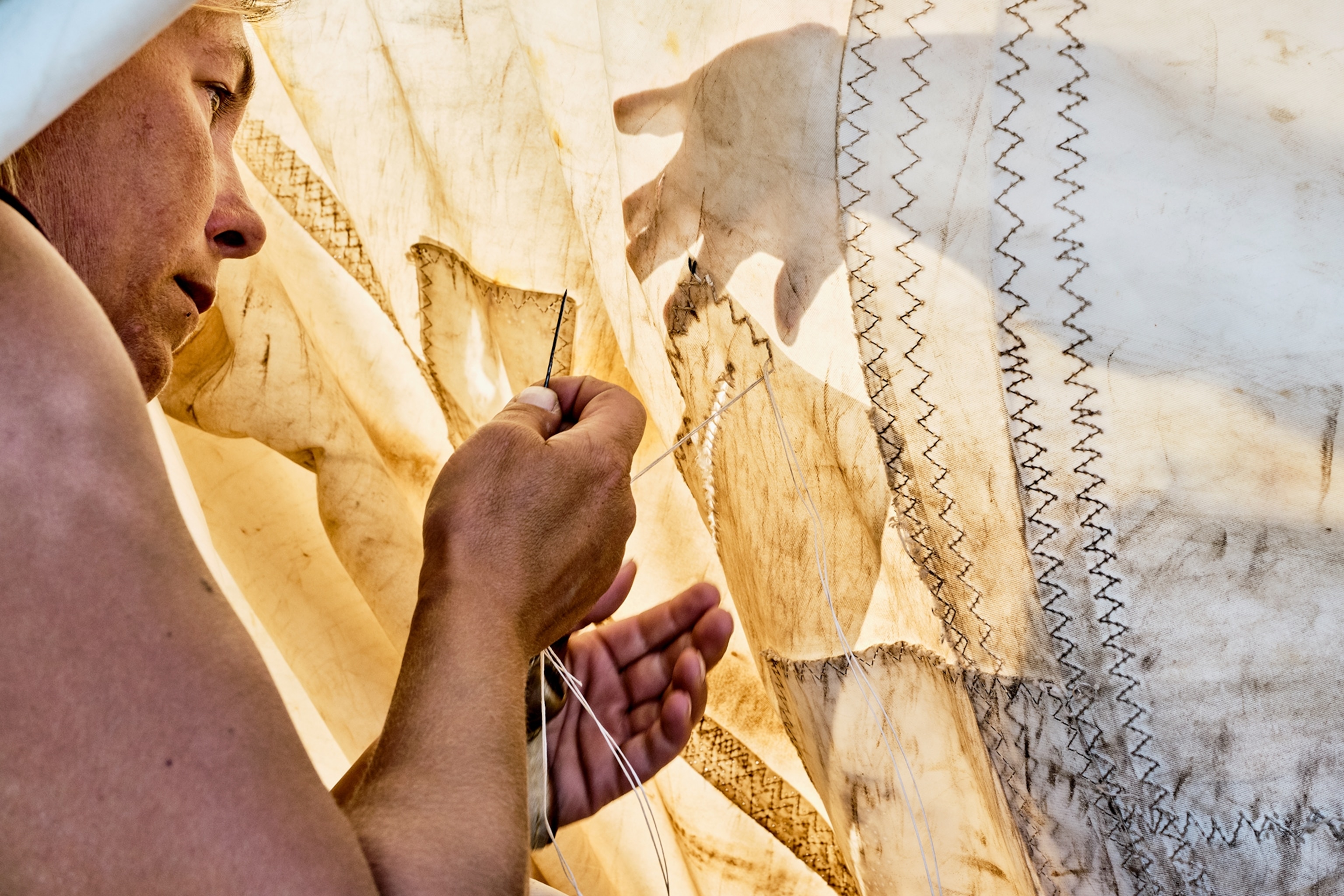 An intimate shot of a woman stitching up an already repaired sail.