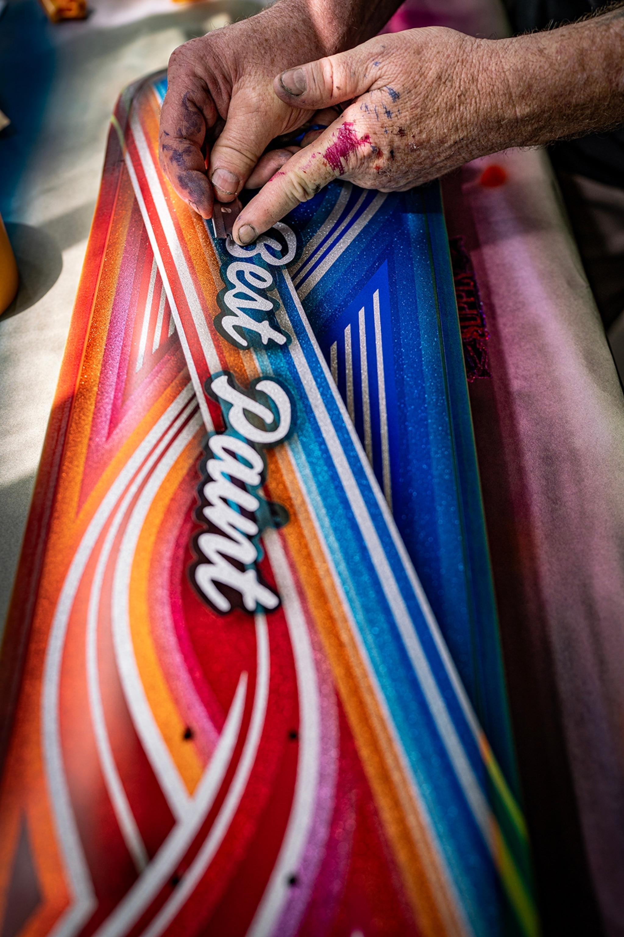 A close-up on a skateboard as a man with inked hands adds finishing touches with a scalpel.