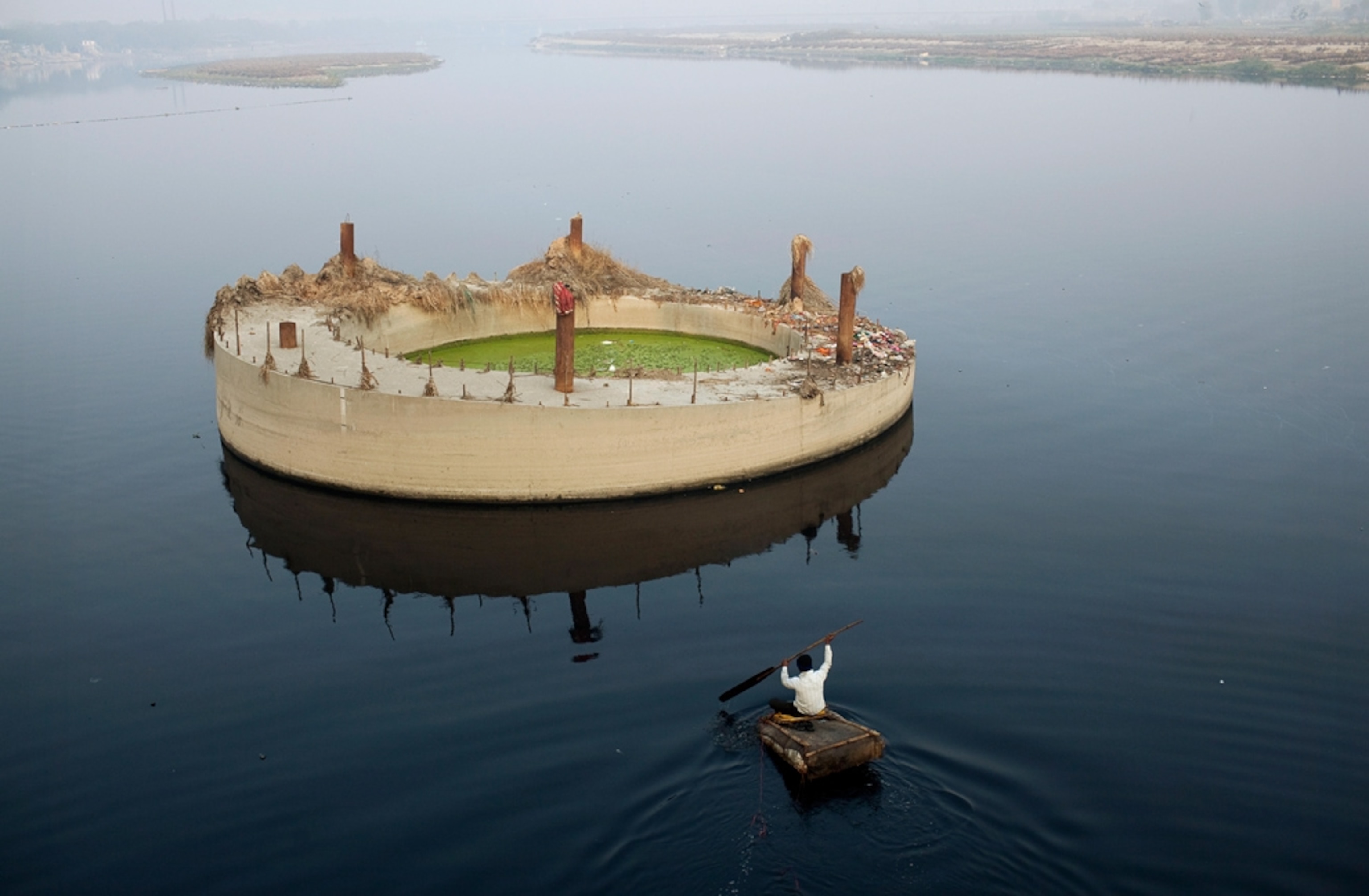 India picture: a man paddling toward a concrete structure in the Yamuna River