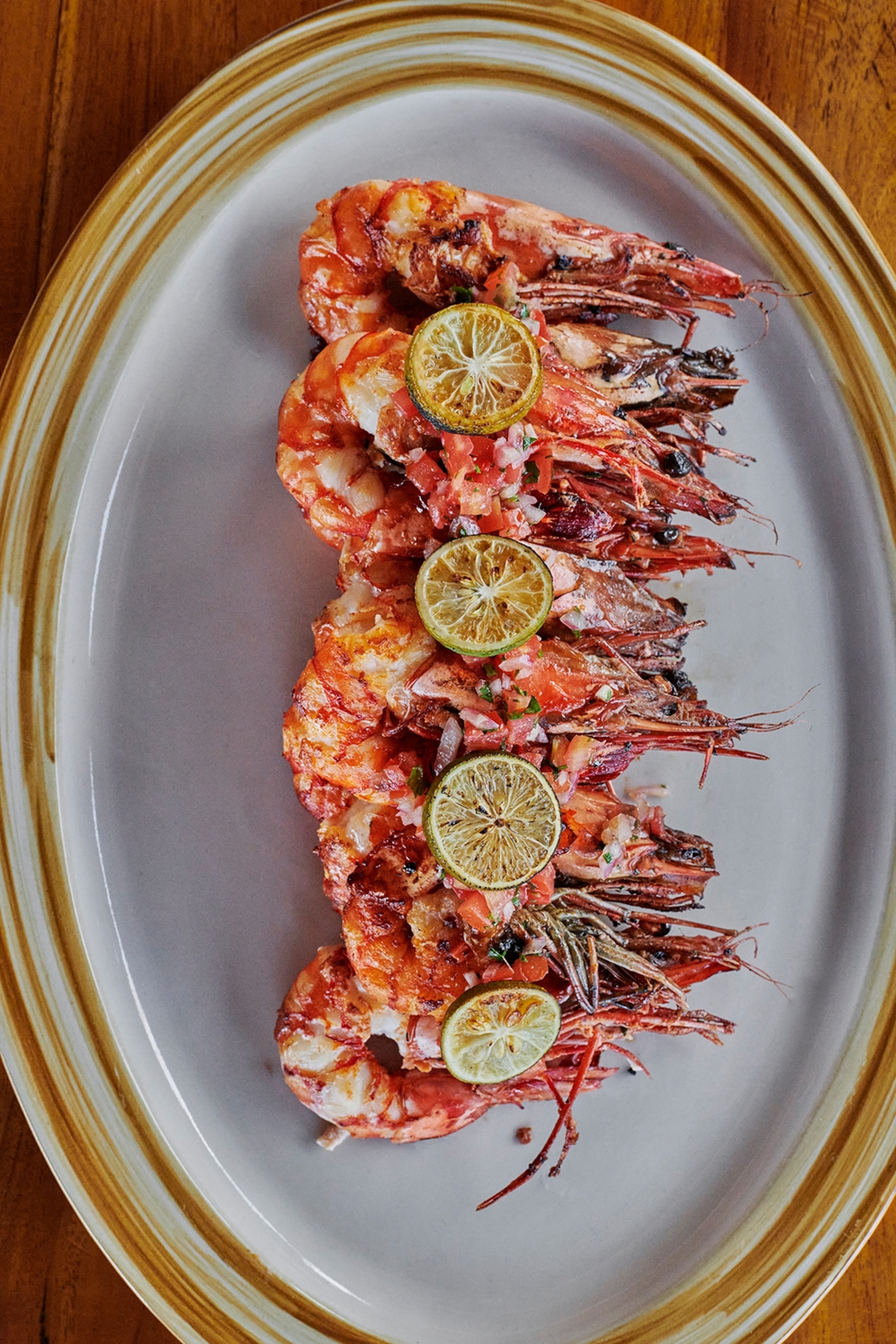 An oval plate of spiced prawns with grilled lime discs on top.