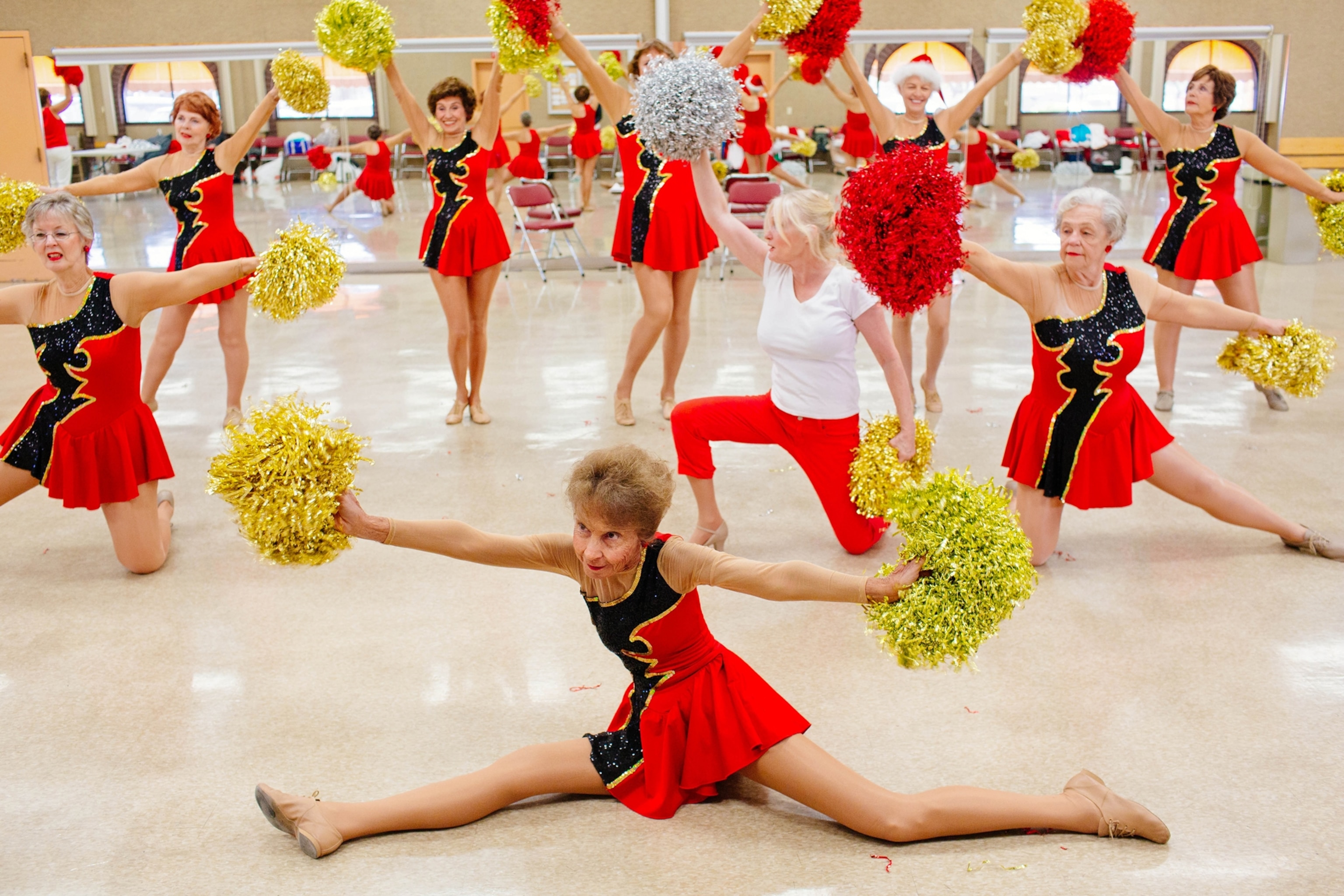 Picture of elderly ladies in short red-and-black dresses dancing with golden pampones.