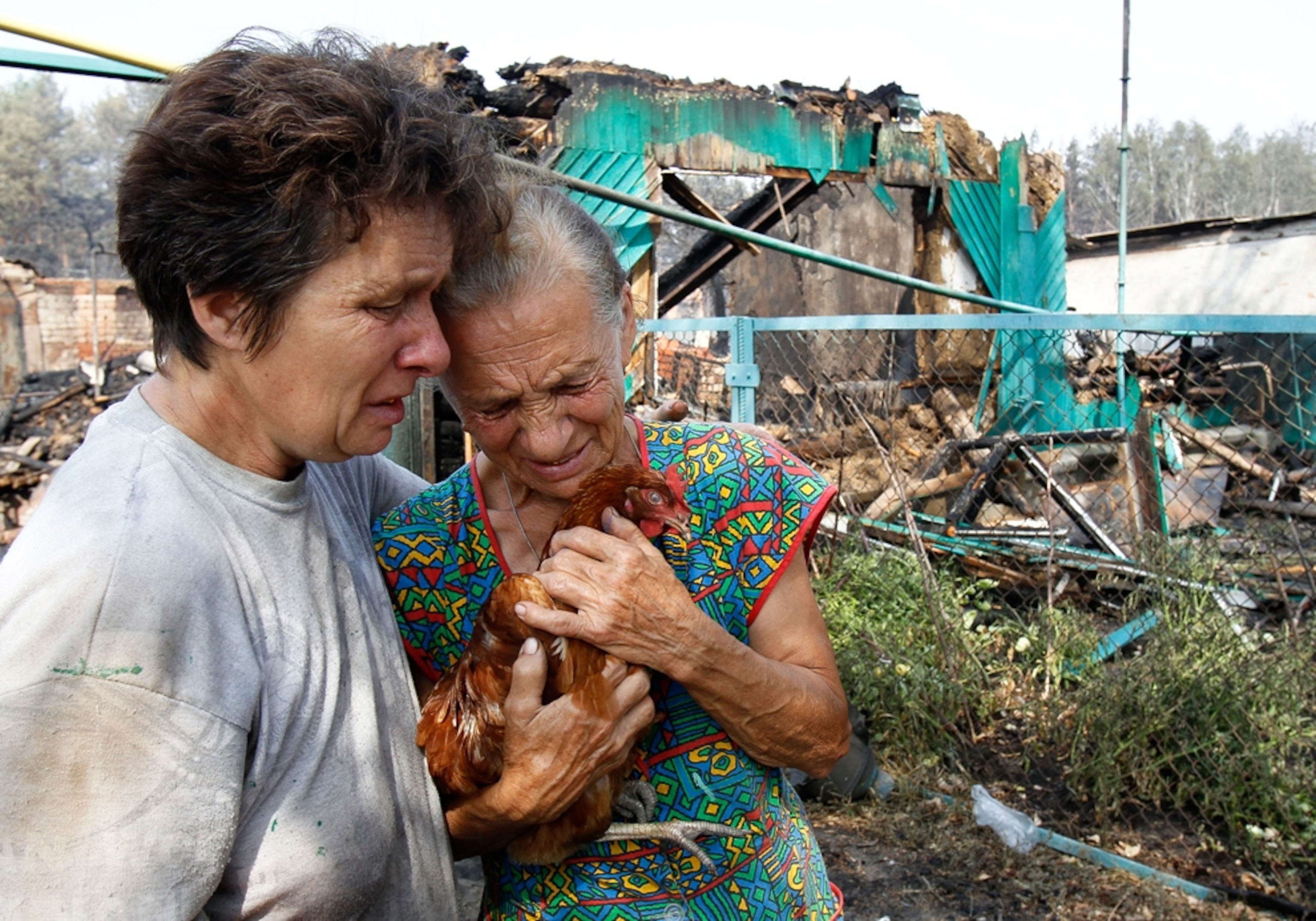 Picture of women in front of a house destroyed by wildfire in Russia, where a record heat wave has sparked hundreds of wildfires.