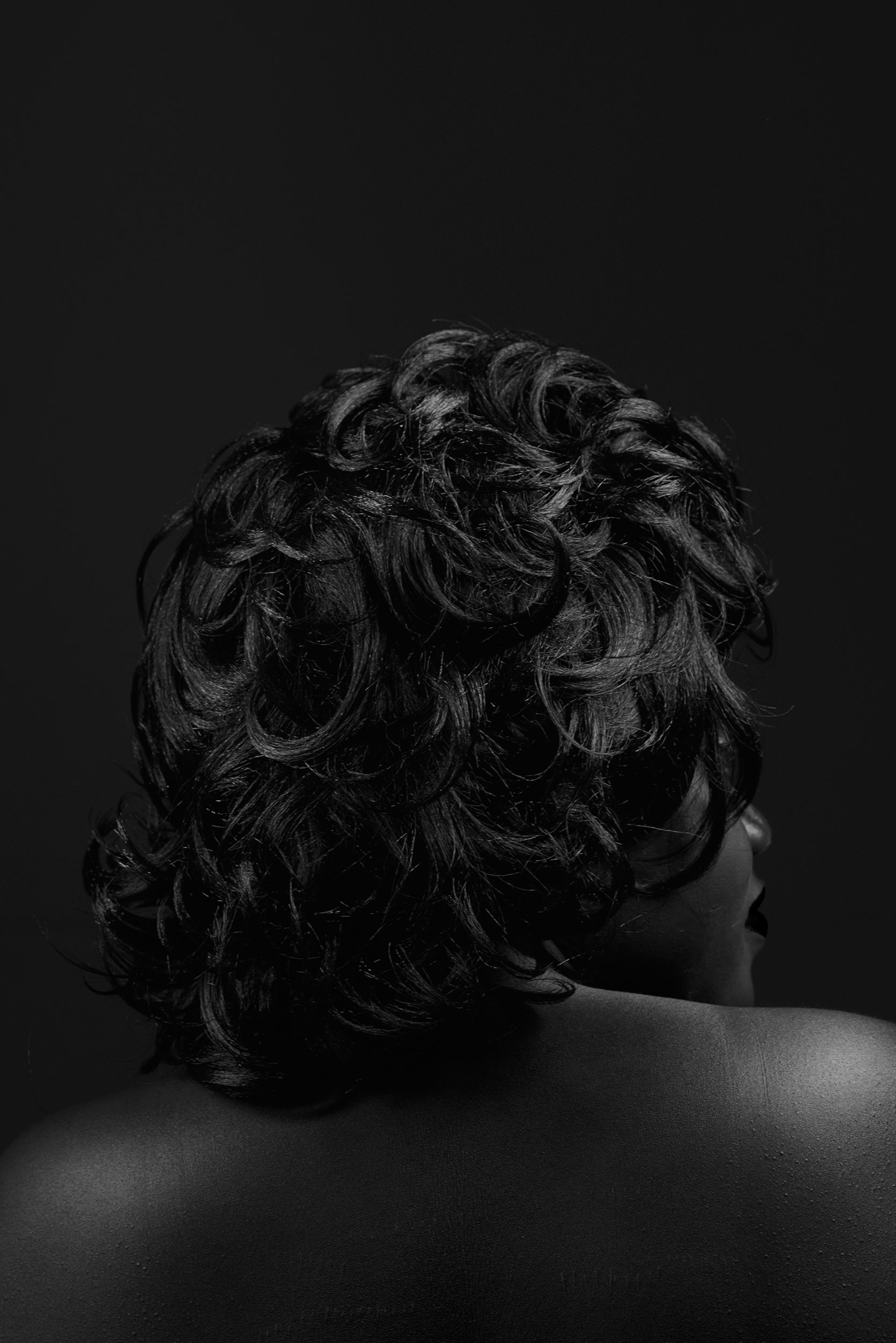 the back of a woman's head, her shoulder-length hair falling in large curls