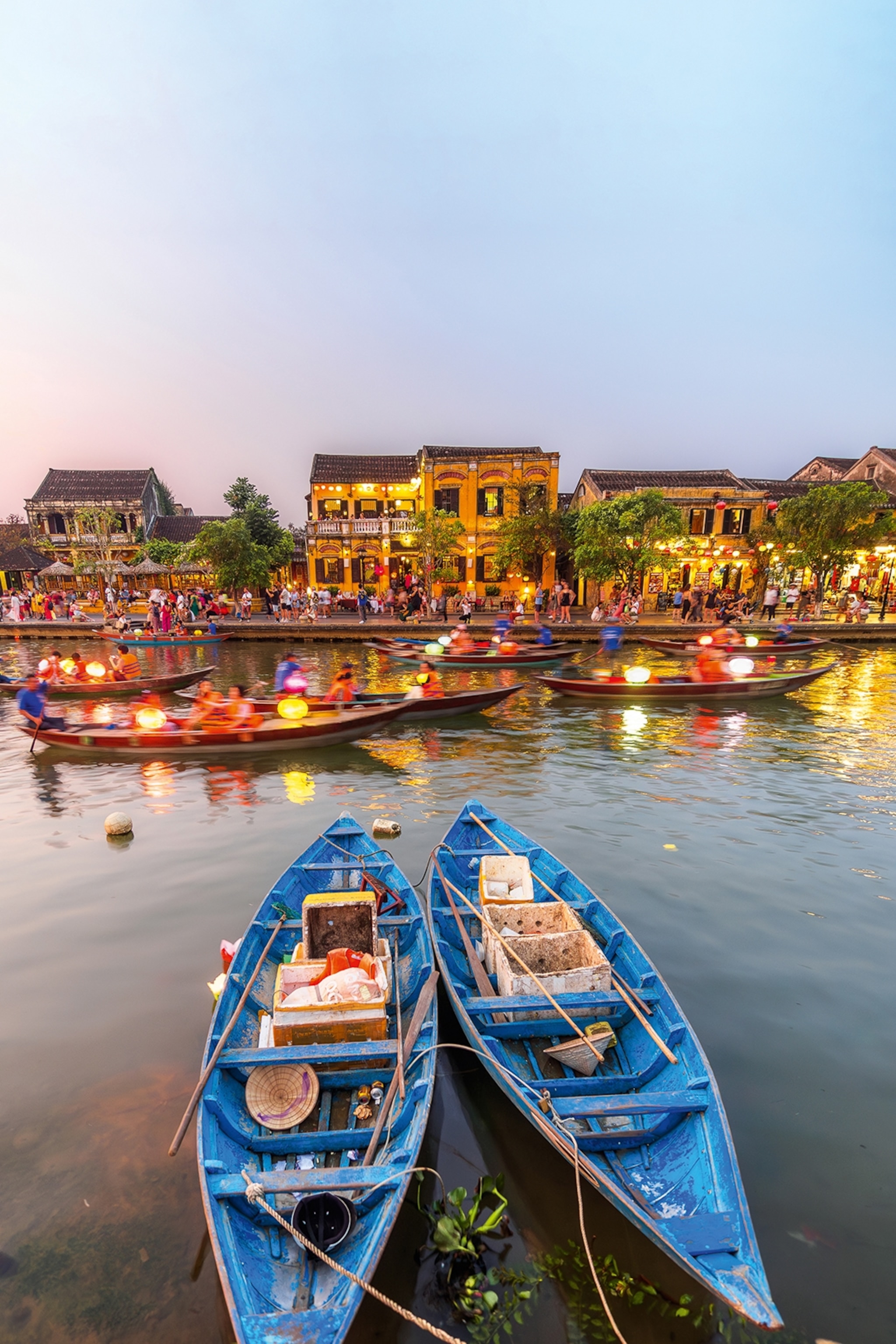 A river with two fishing boats anchored on the shore and small houses lining the other riverbank.