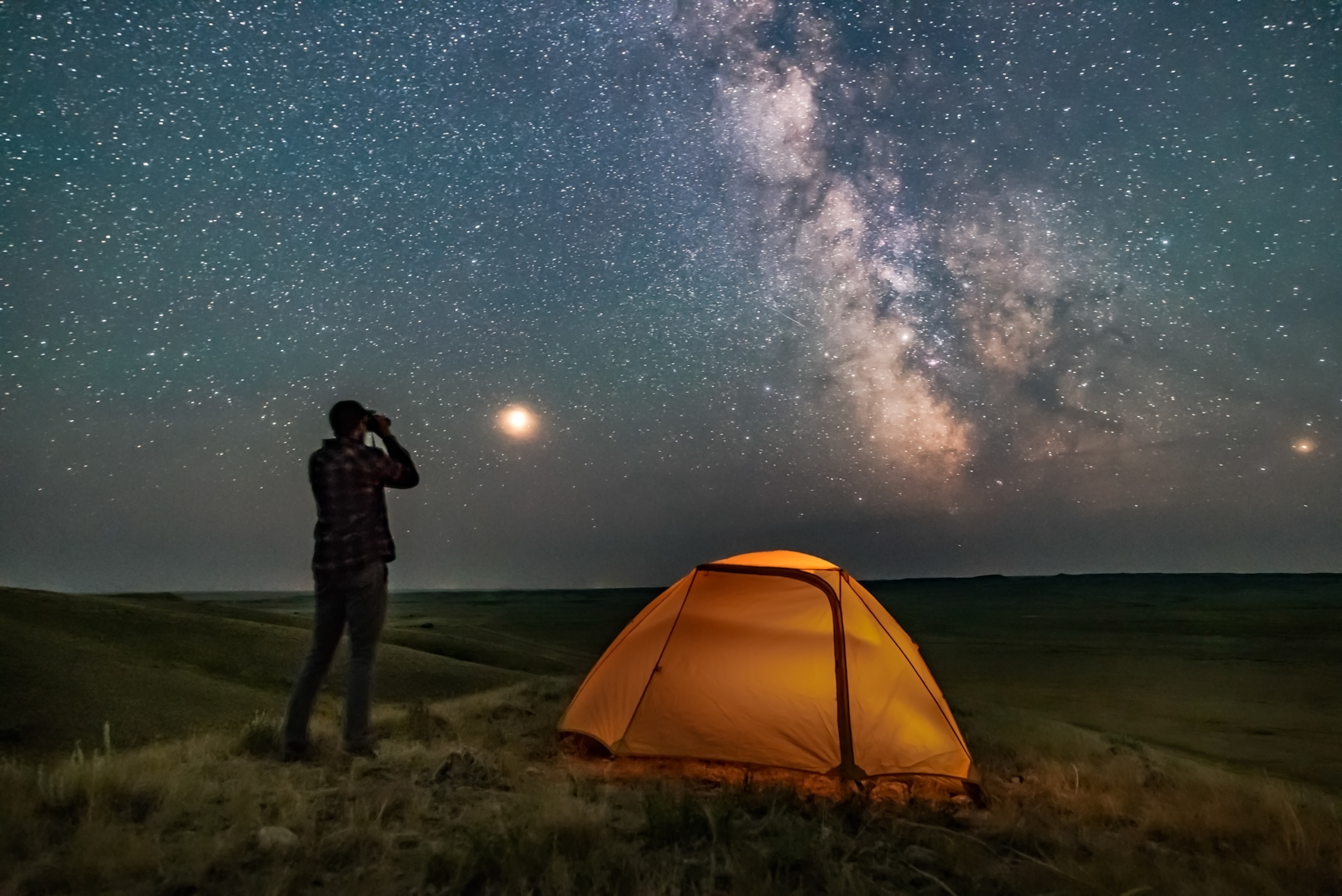 A person poses for a scene in Grasslands National Park, Saskatchewan, of stargazing with binoculars under the Milky Way