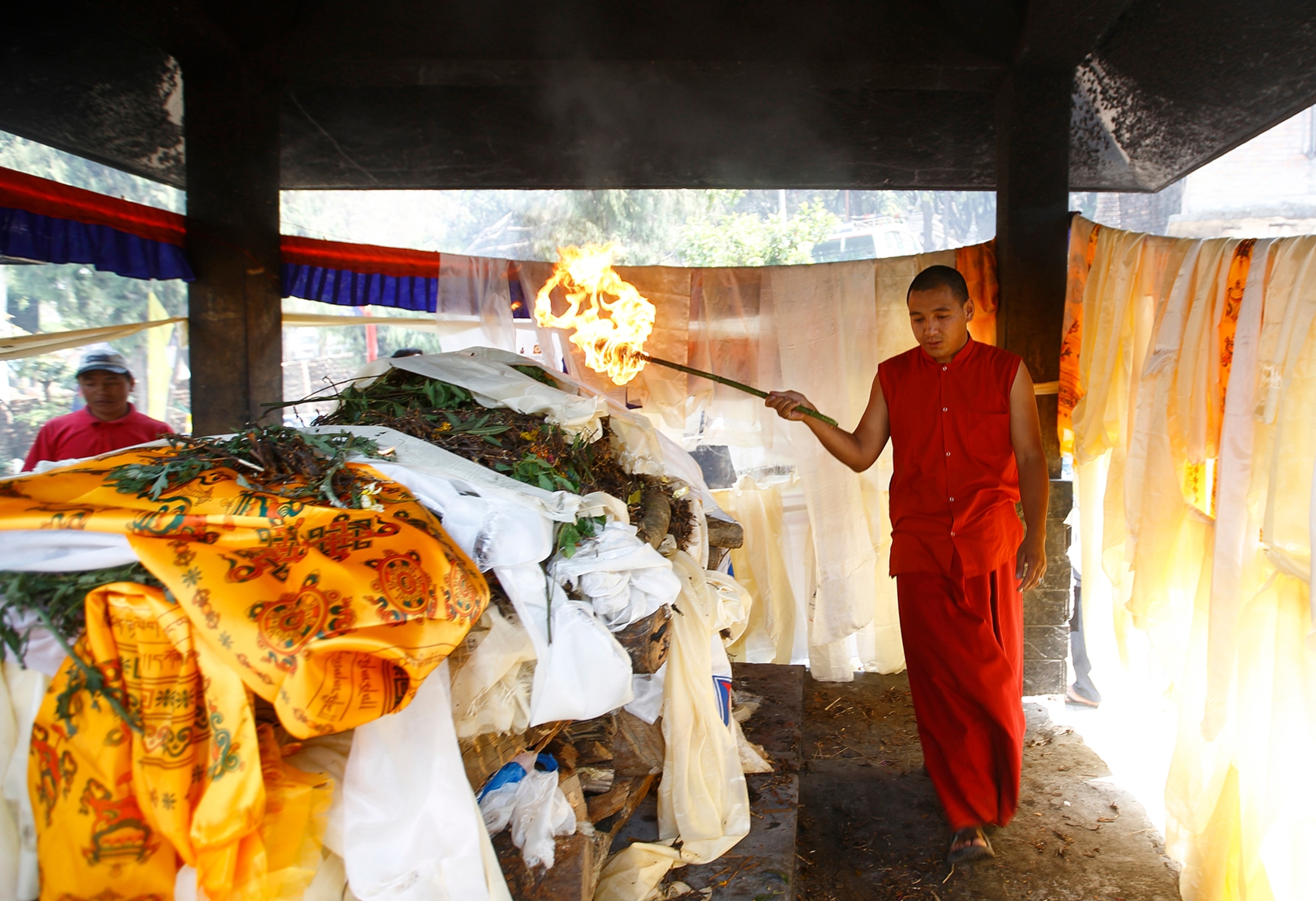 a monk setting fire to the body of a sherpa during a cremation ceremony.