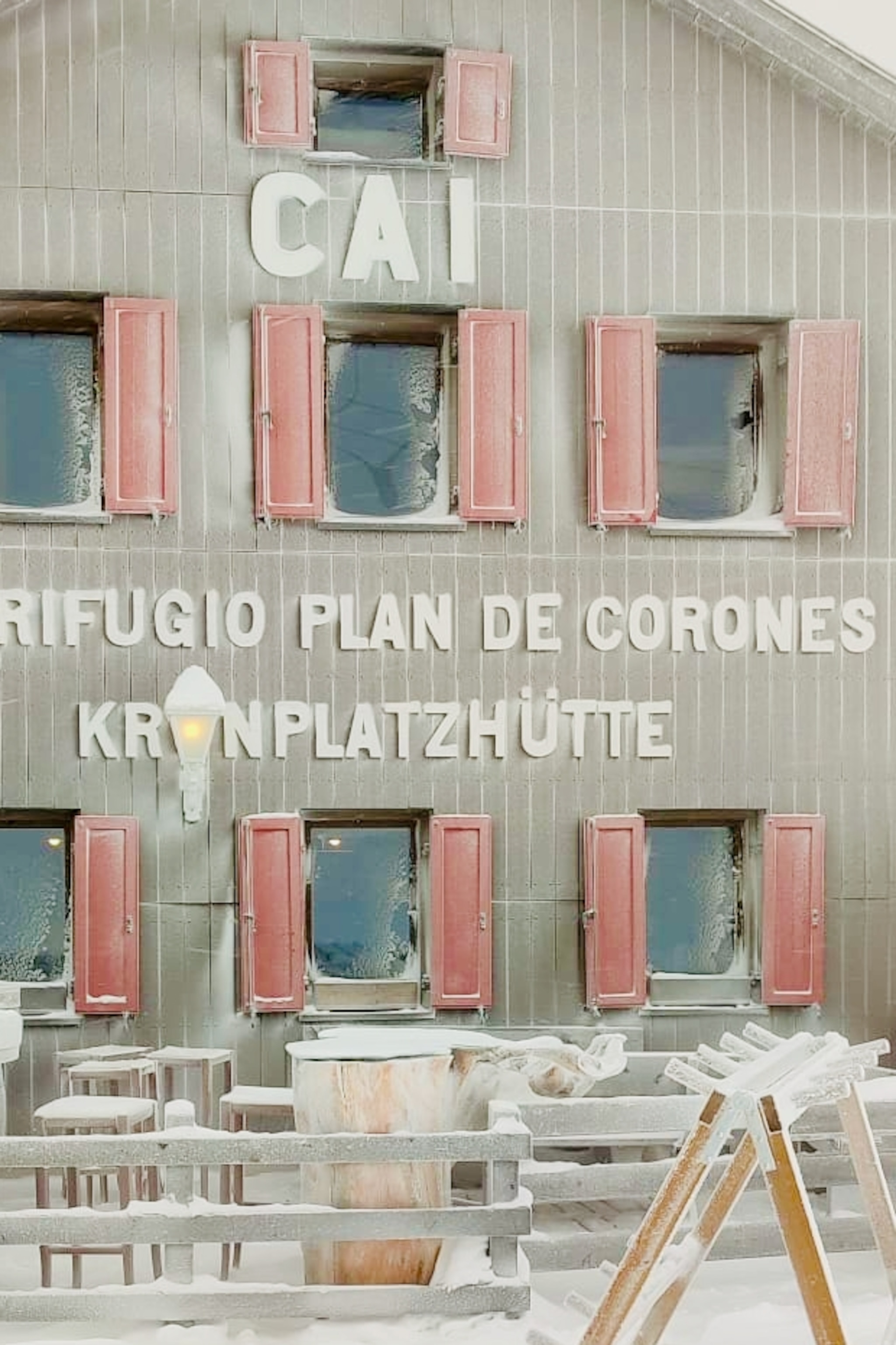 The fassade of a wooden ski hut with shutters and big lettering across the front.