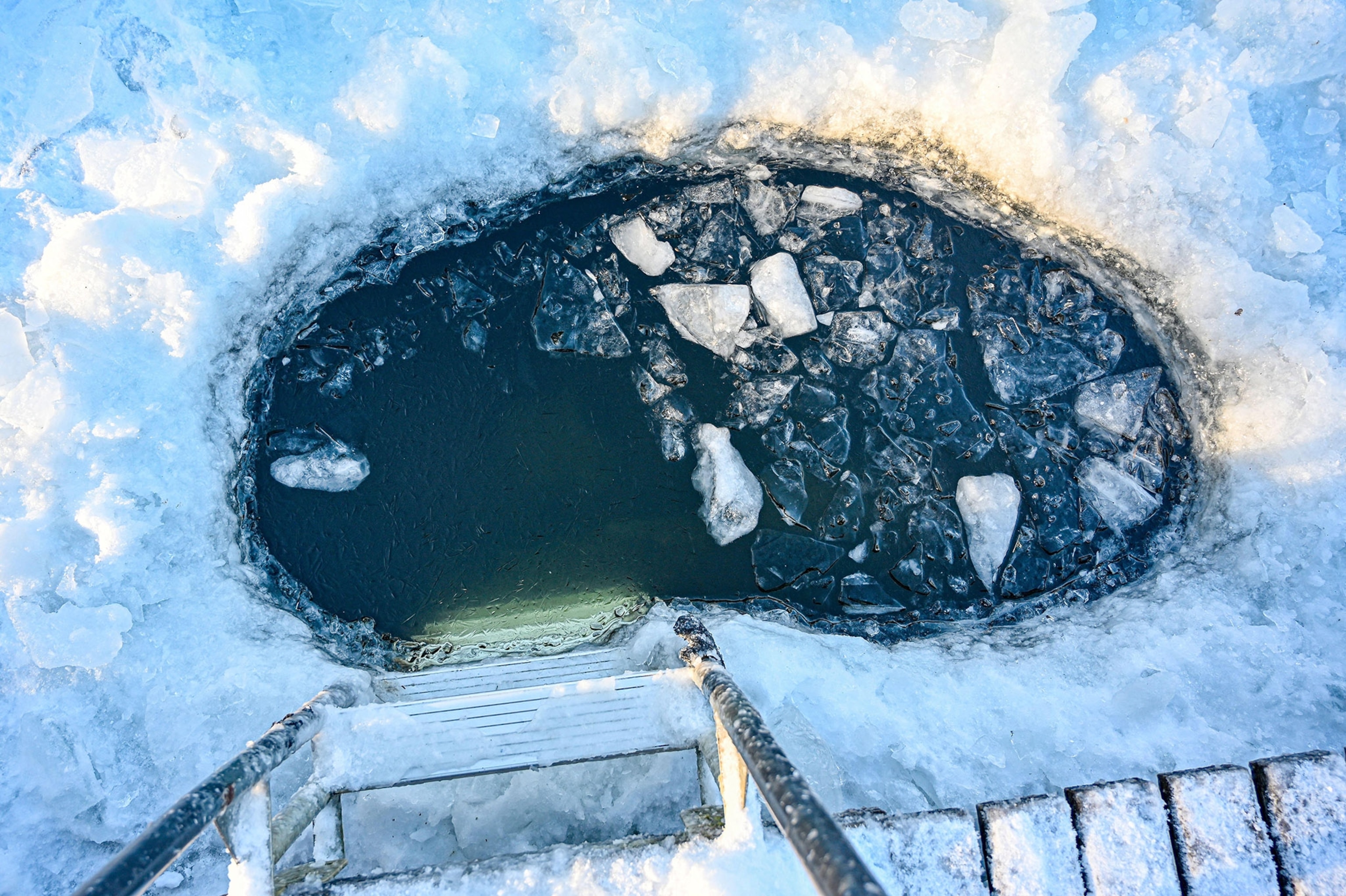 A ladder descends into a hole in a frozen lake.