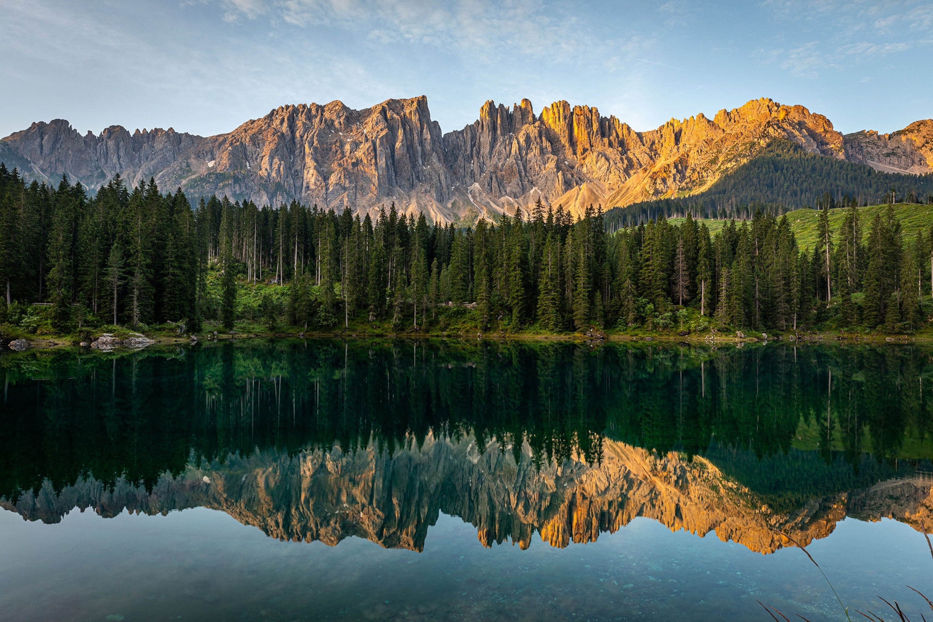 A mountain range reflected in a clear lake with pine trees.