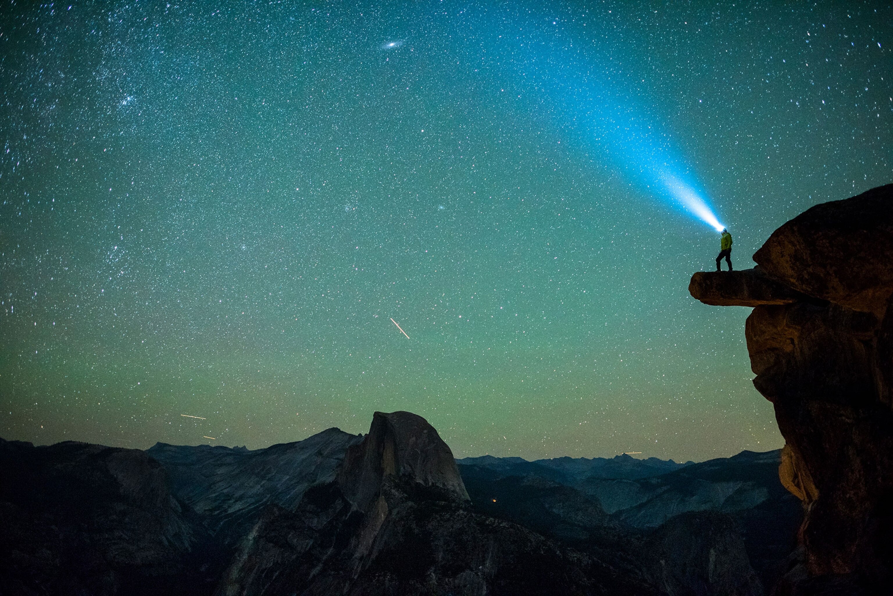 a man standing on an overhanging rock with the Half Dome in the background