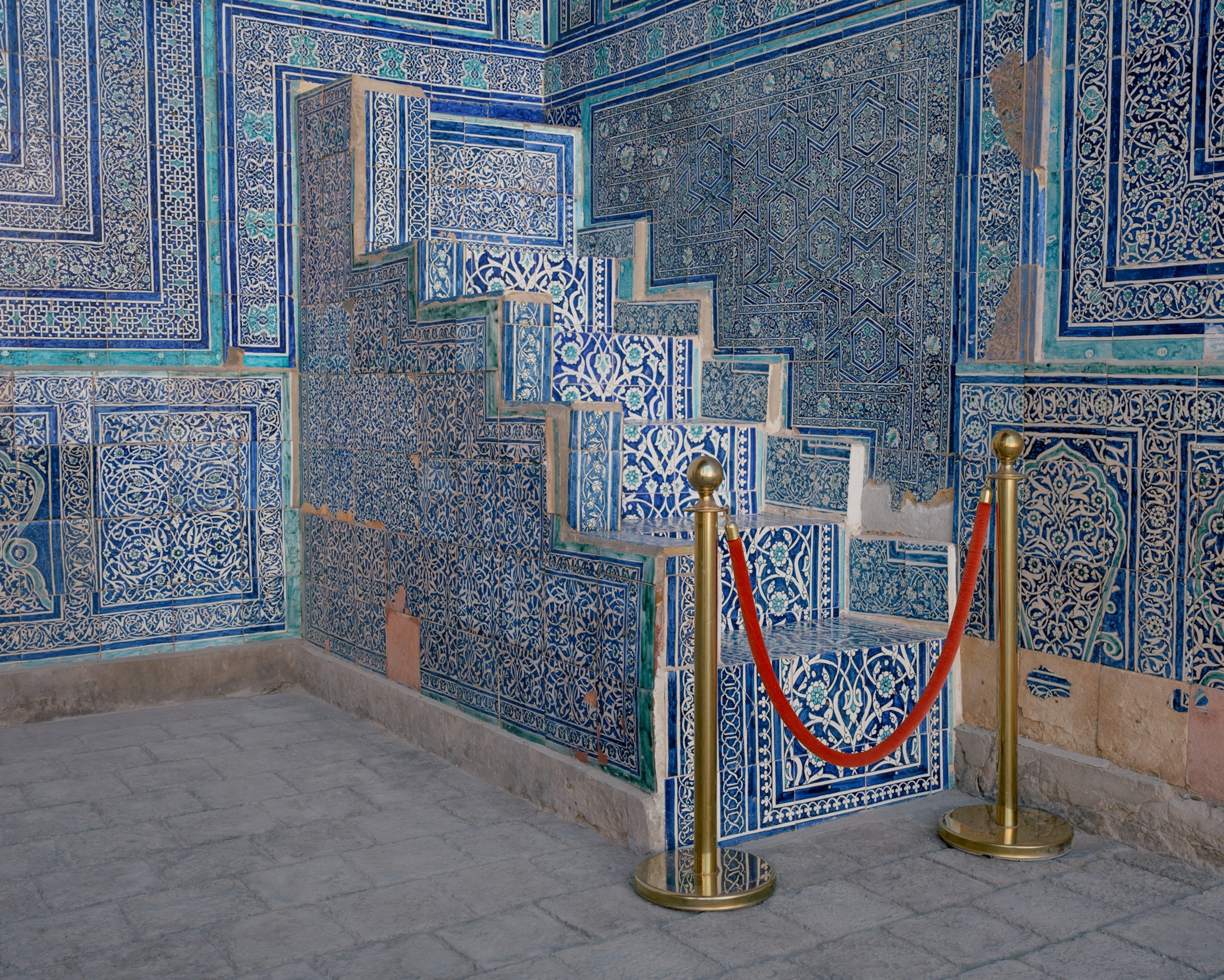 The corner of two walls with stairs, leading nowhere but into the well, in the corner. They are made of intricate, rosy blue tiles and are blocked by a red velvet rope.