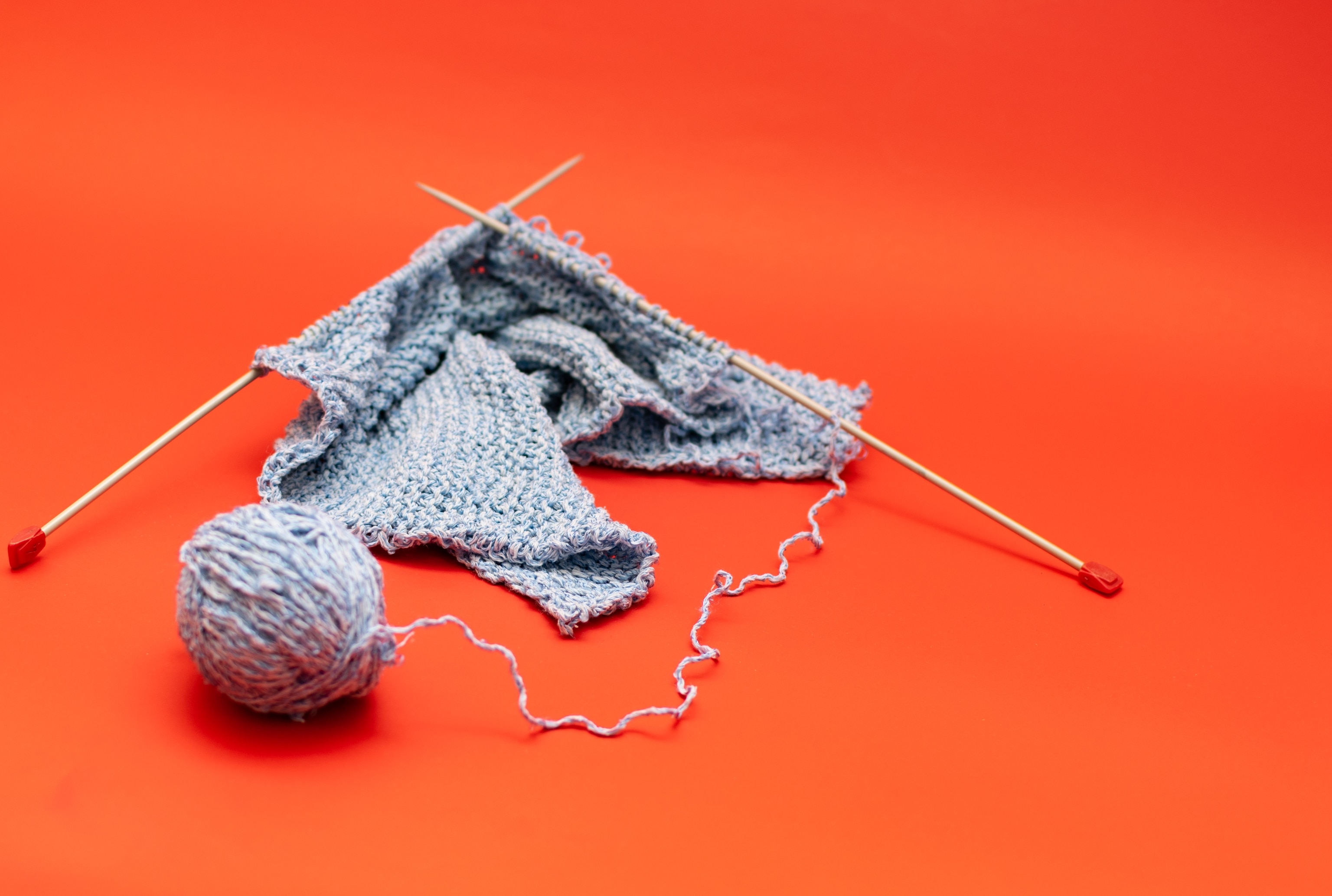a blue ball of yarn and knitting needles on an orange background