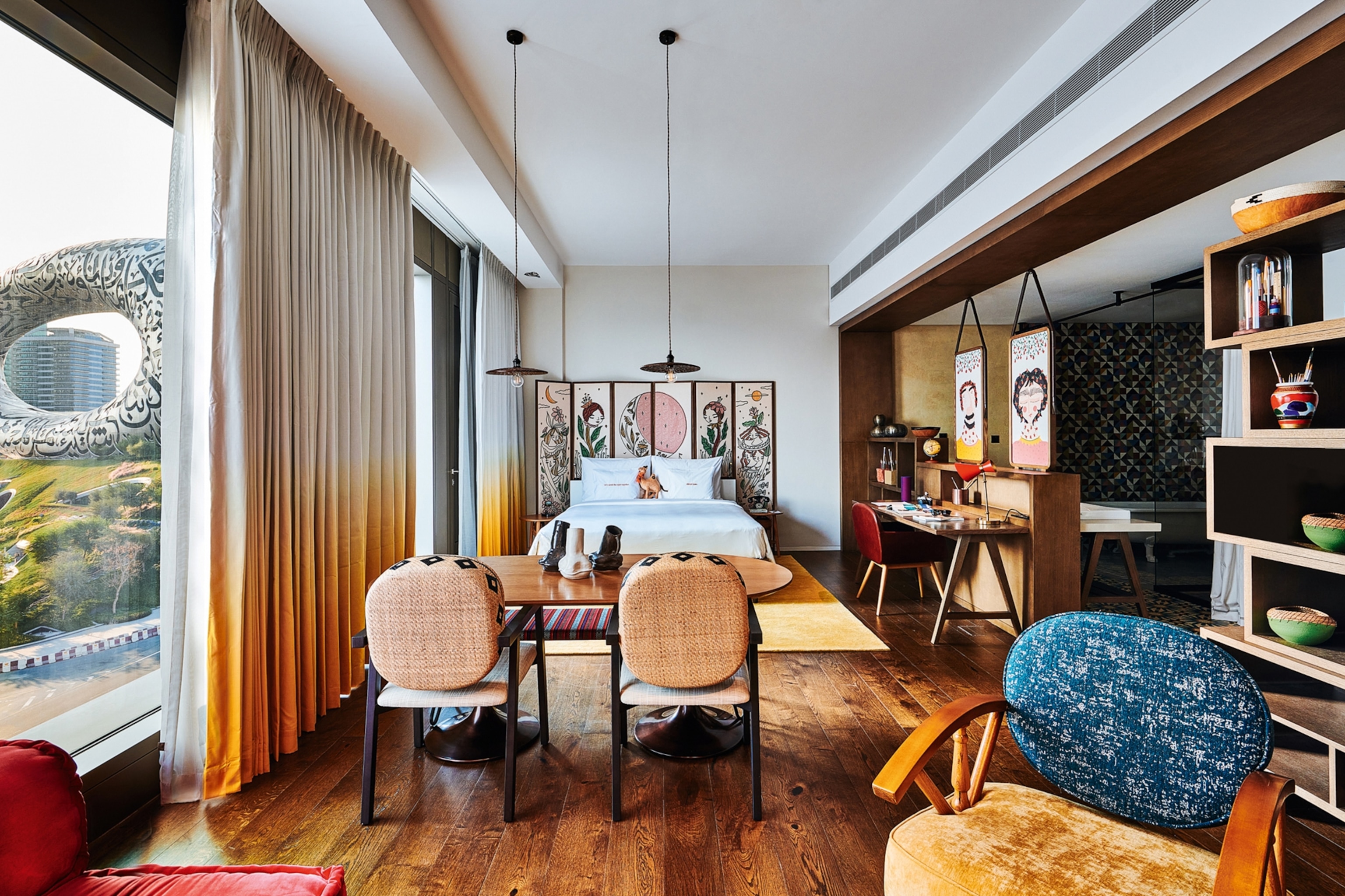 An open-plan, flat-like hotel bedroom with adjacent kitchen, lounging area and dining table.