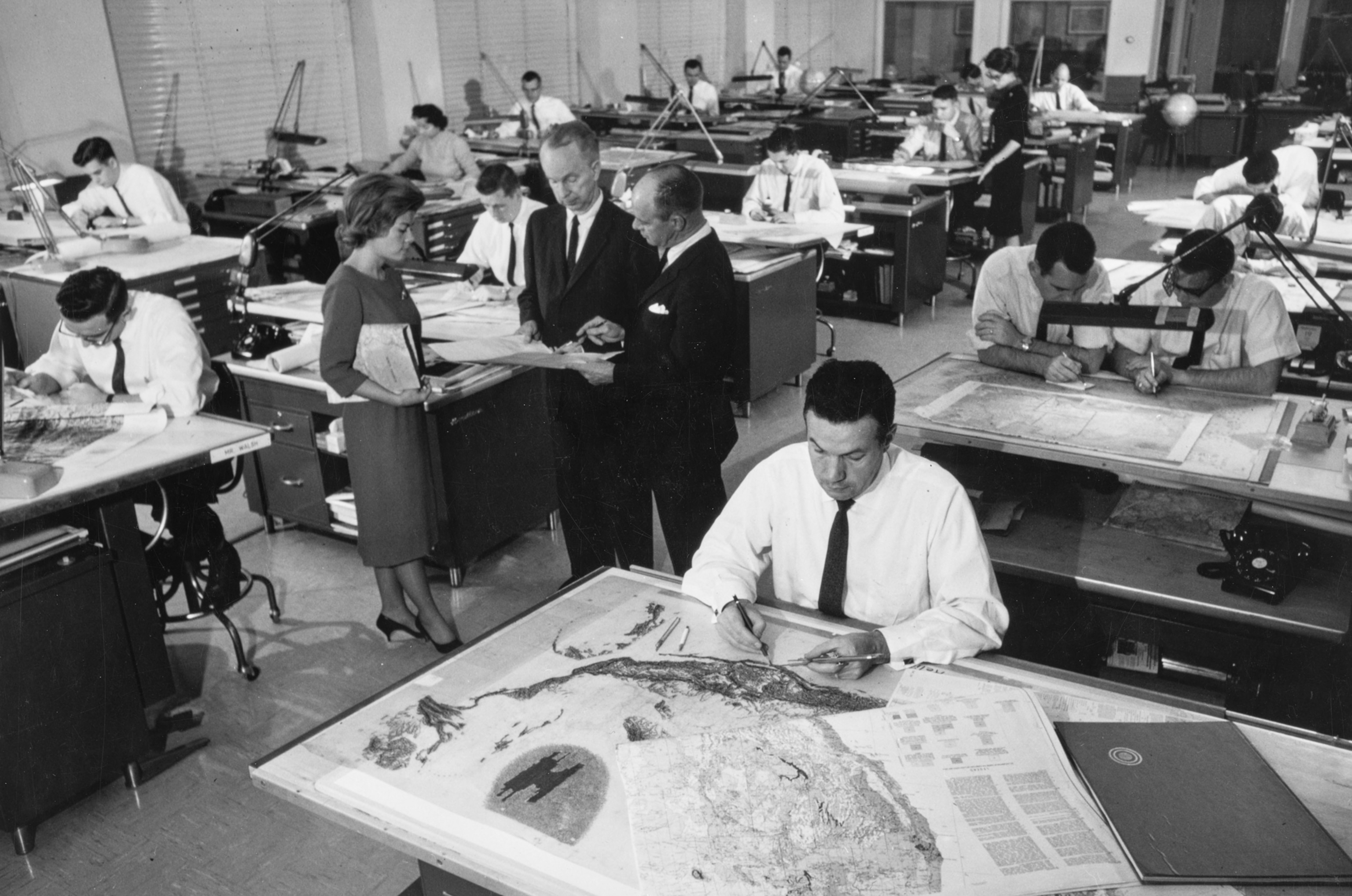 business A large room of people at desks working on maps