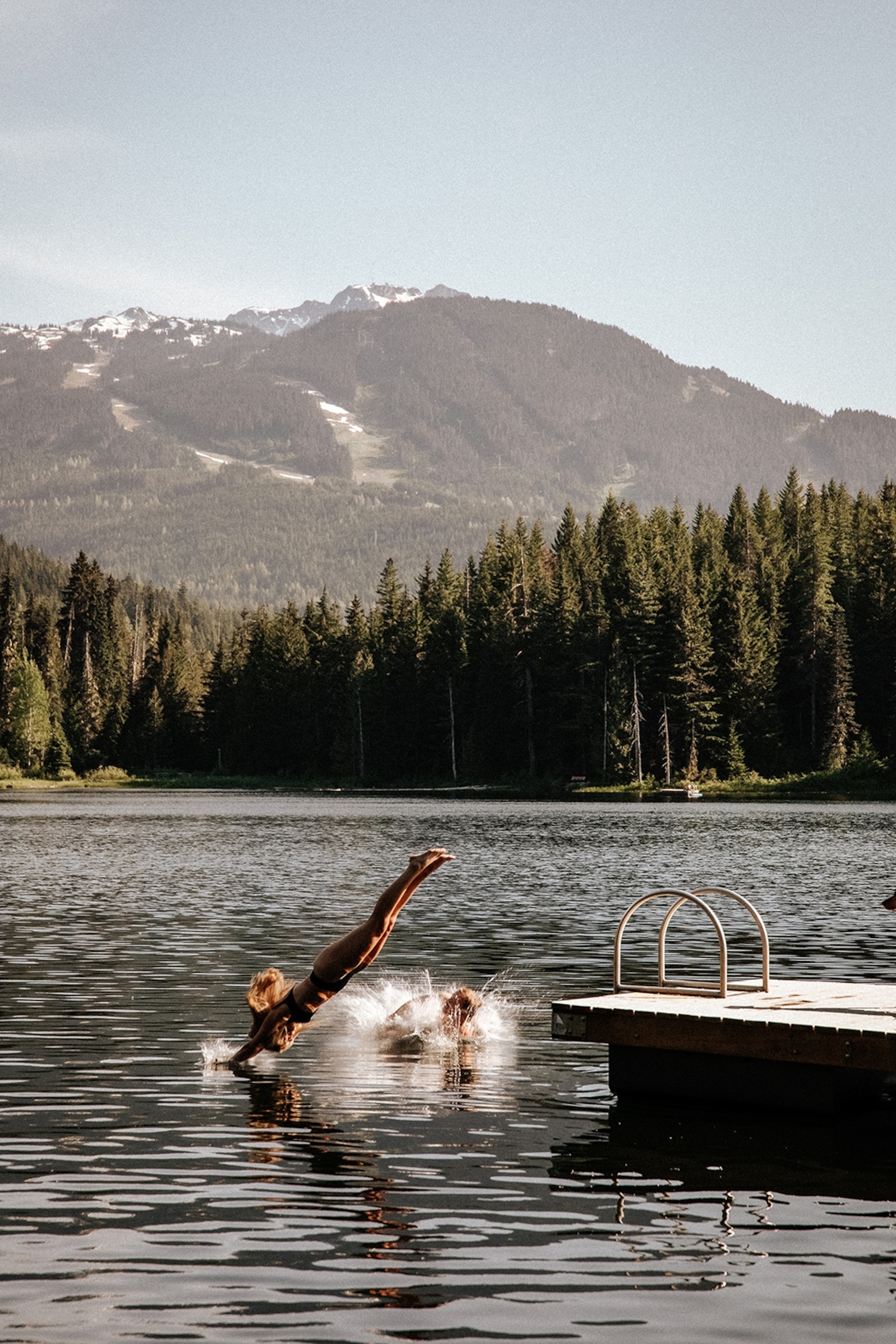A couple of people jumping into a mountain lake from a pier.