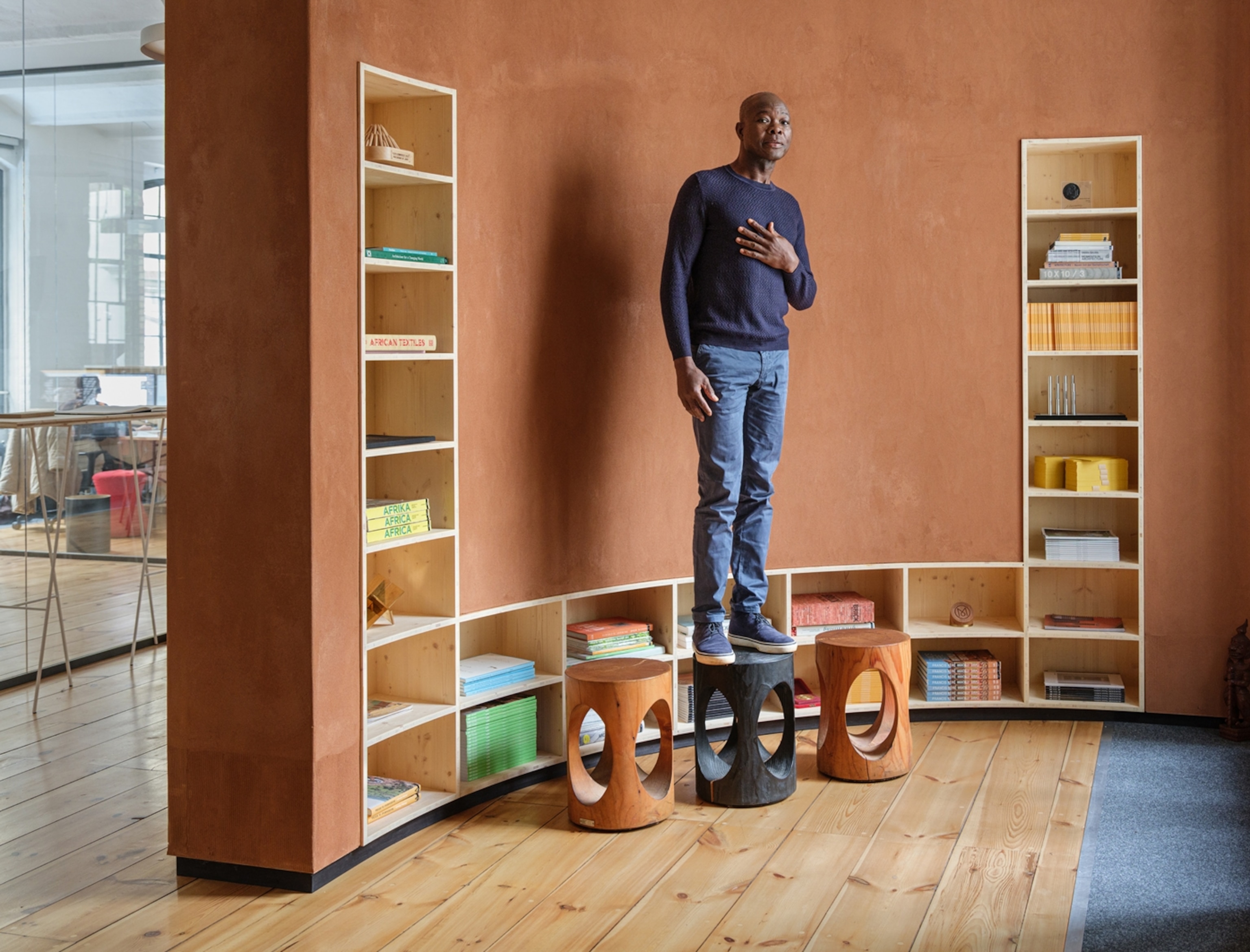 A man stands for a portrait in an orange room with books