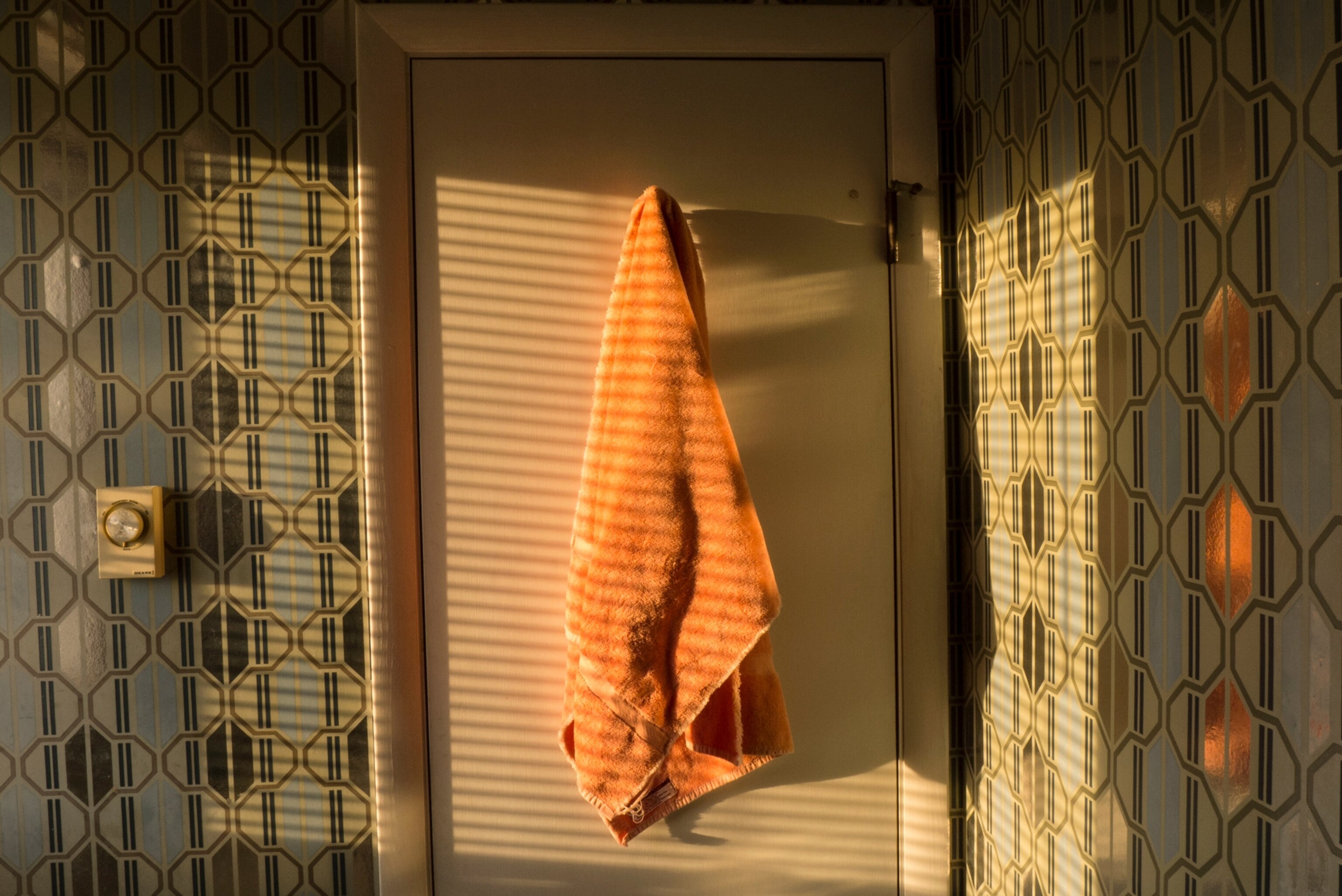 an orange town hanging on the back of a door, bathed in golden light coming through the blinds