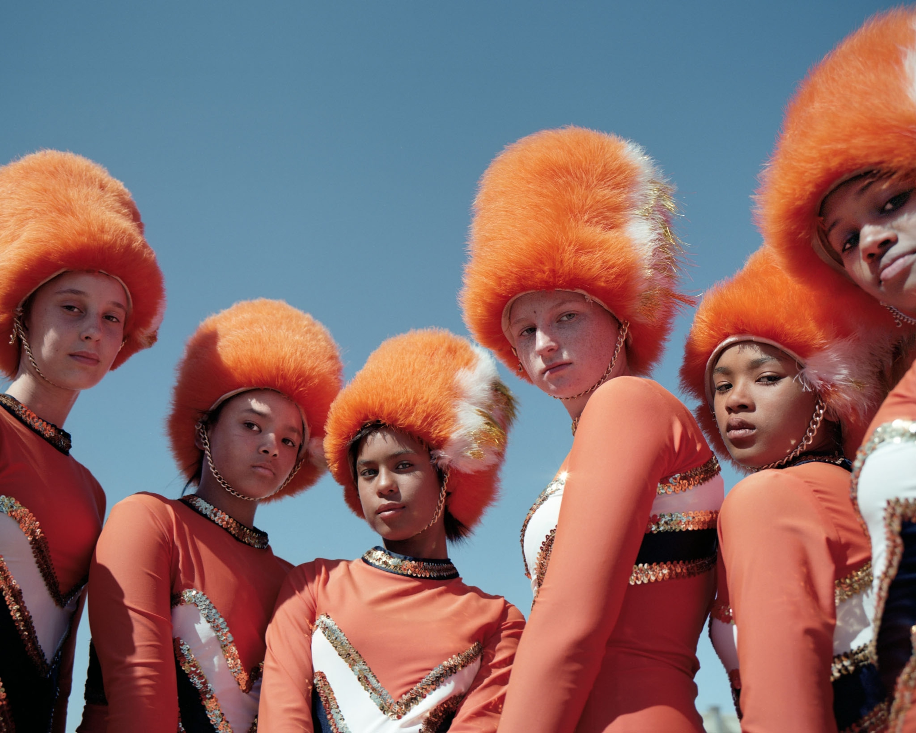 six young women in orange uniforms against a blue sky