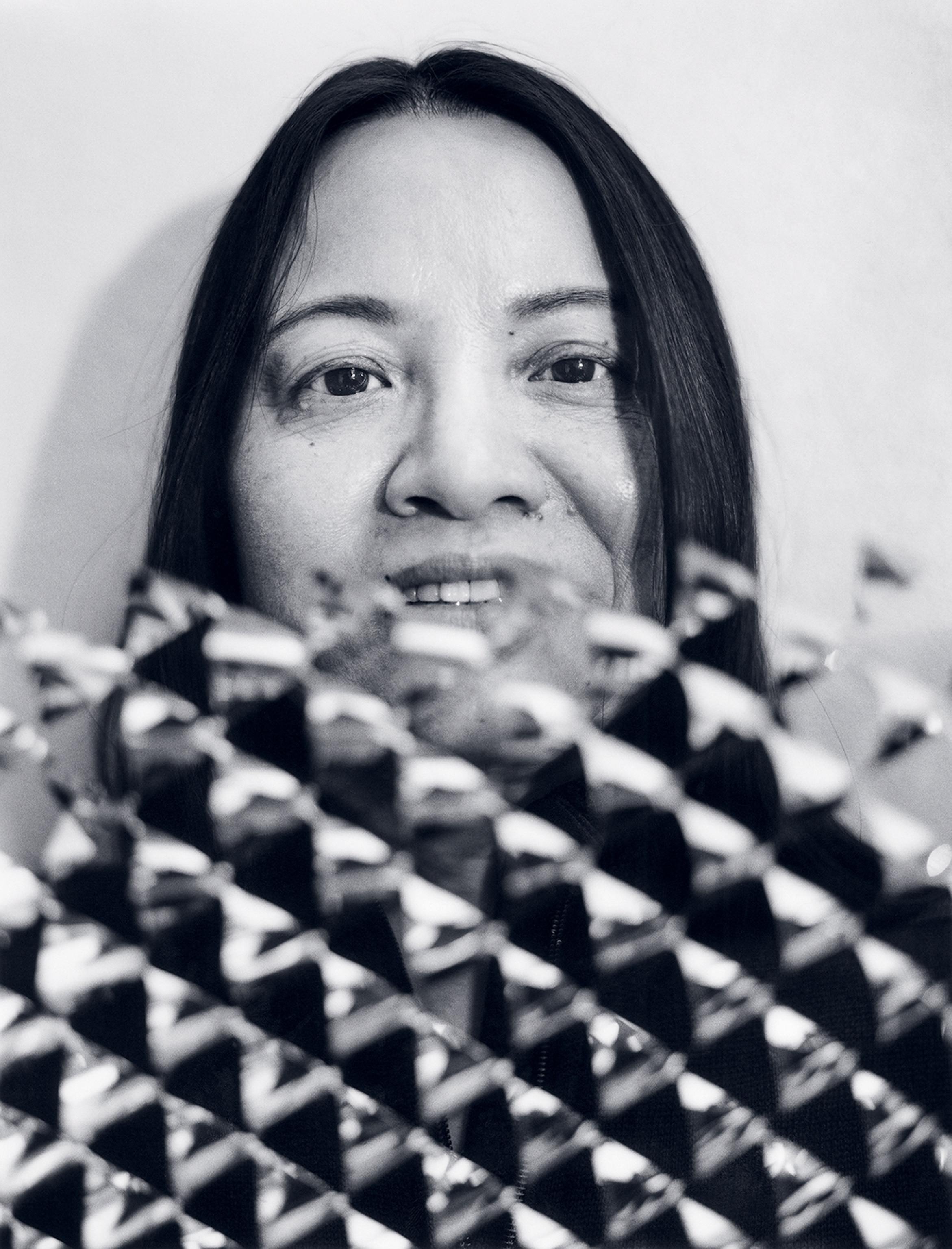 A black and white portrait of a woman who is holding up a patterned object which is covering the lower half of the frame.