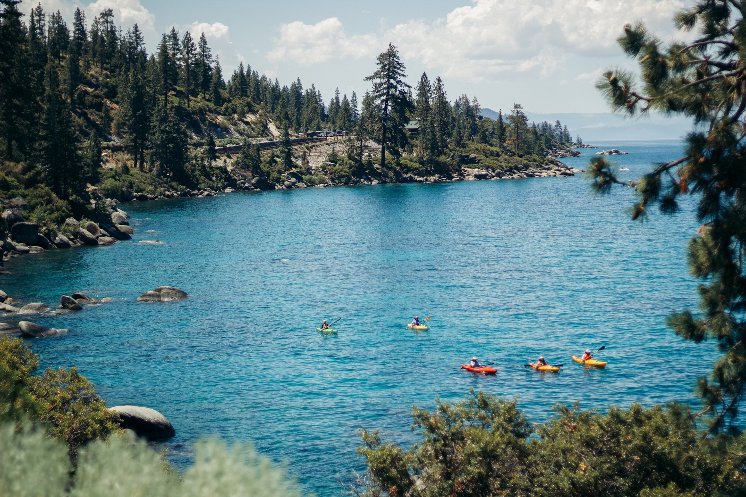 People kayak in a blue water lake with trees on the shoreline