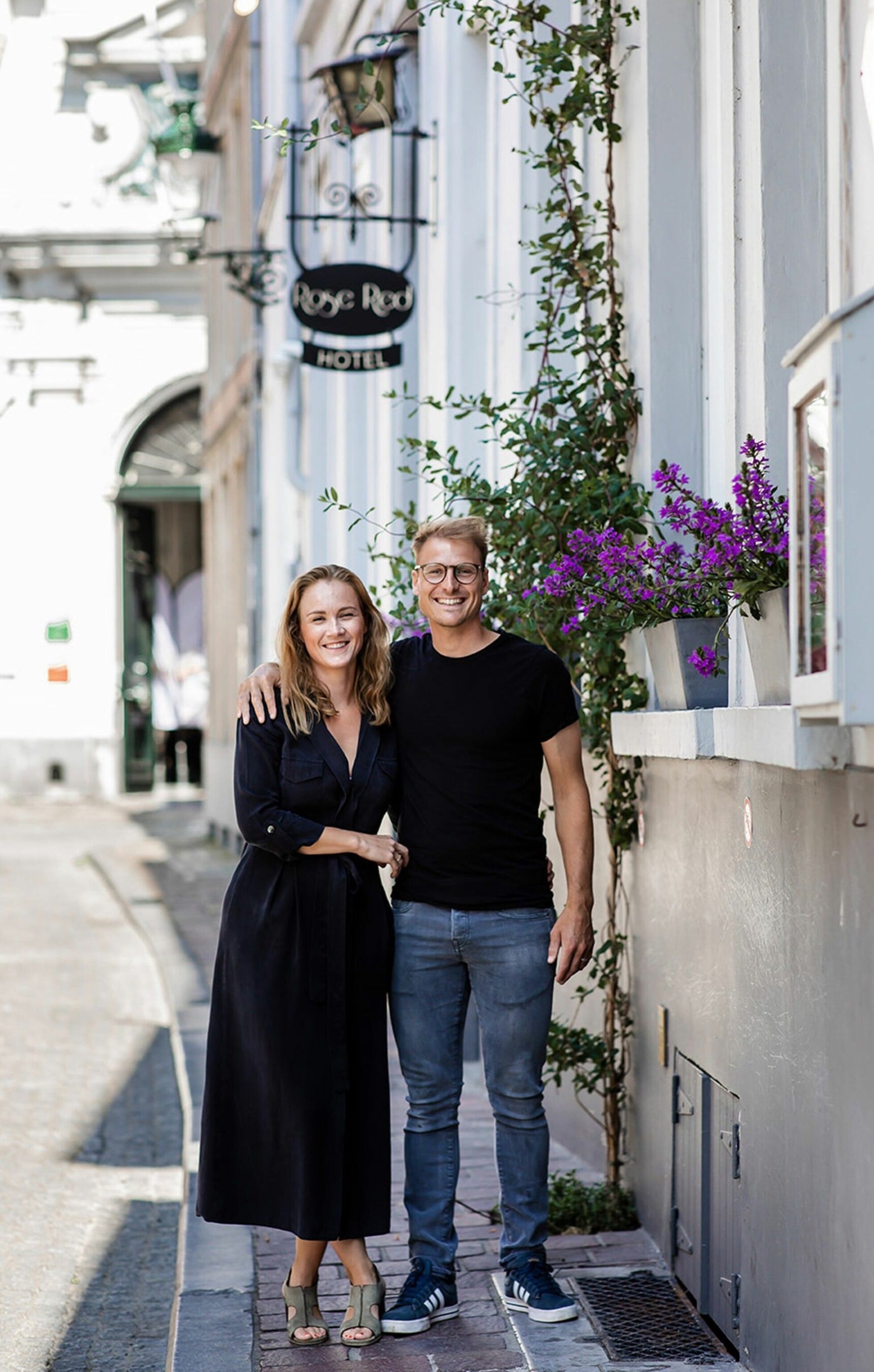 Jannetien and Korneel stand outside Café Rose Red. They are both blonde and wearing dark clothing.