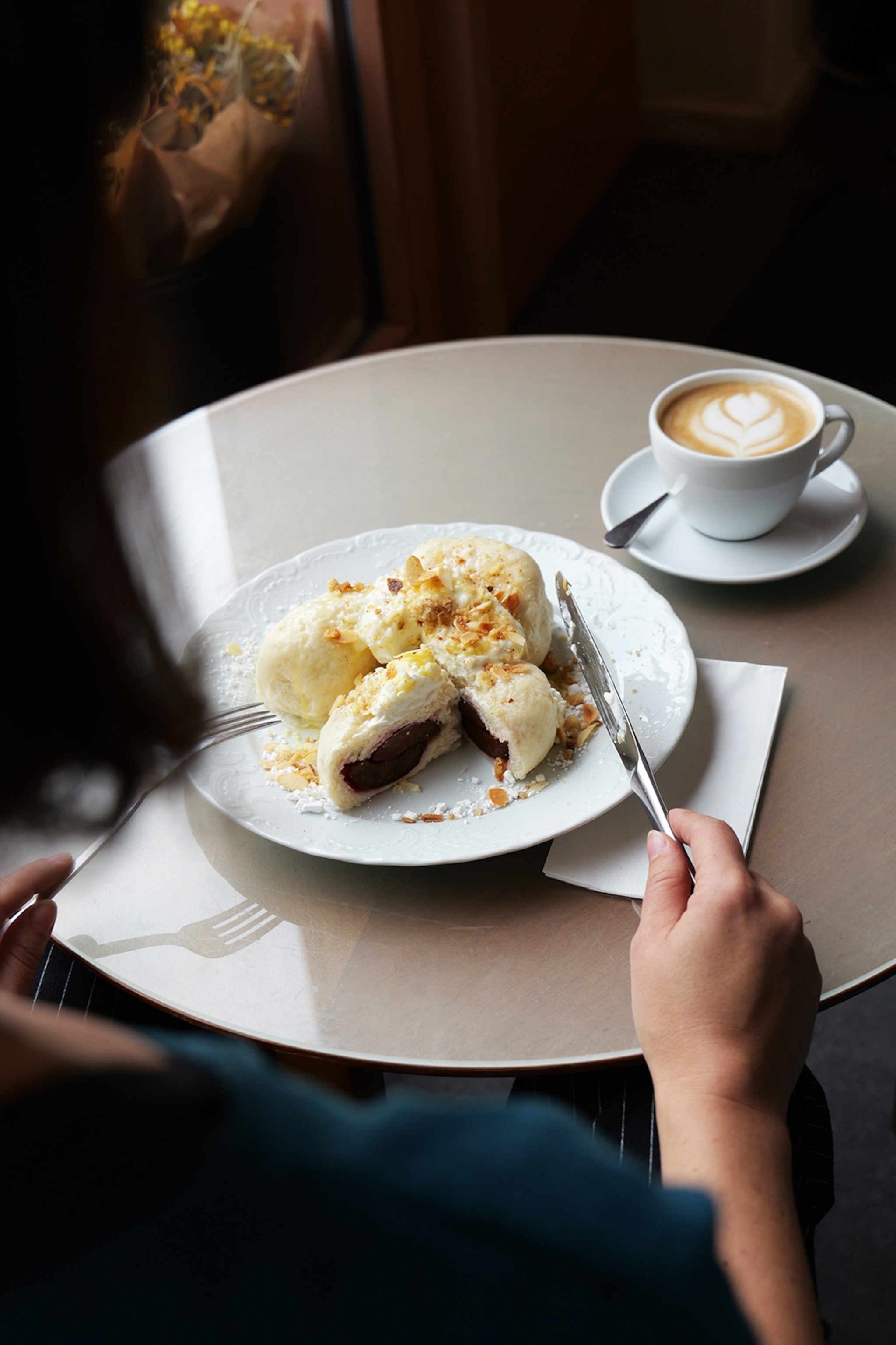A plate of plum-filled dumplings shot over the shoulder of a female diner in a cafe.
