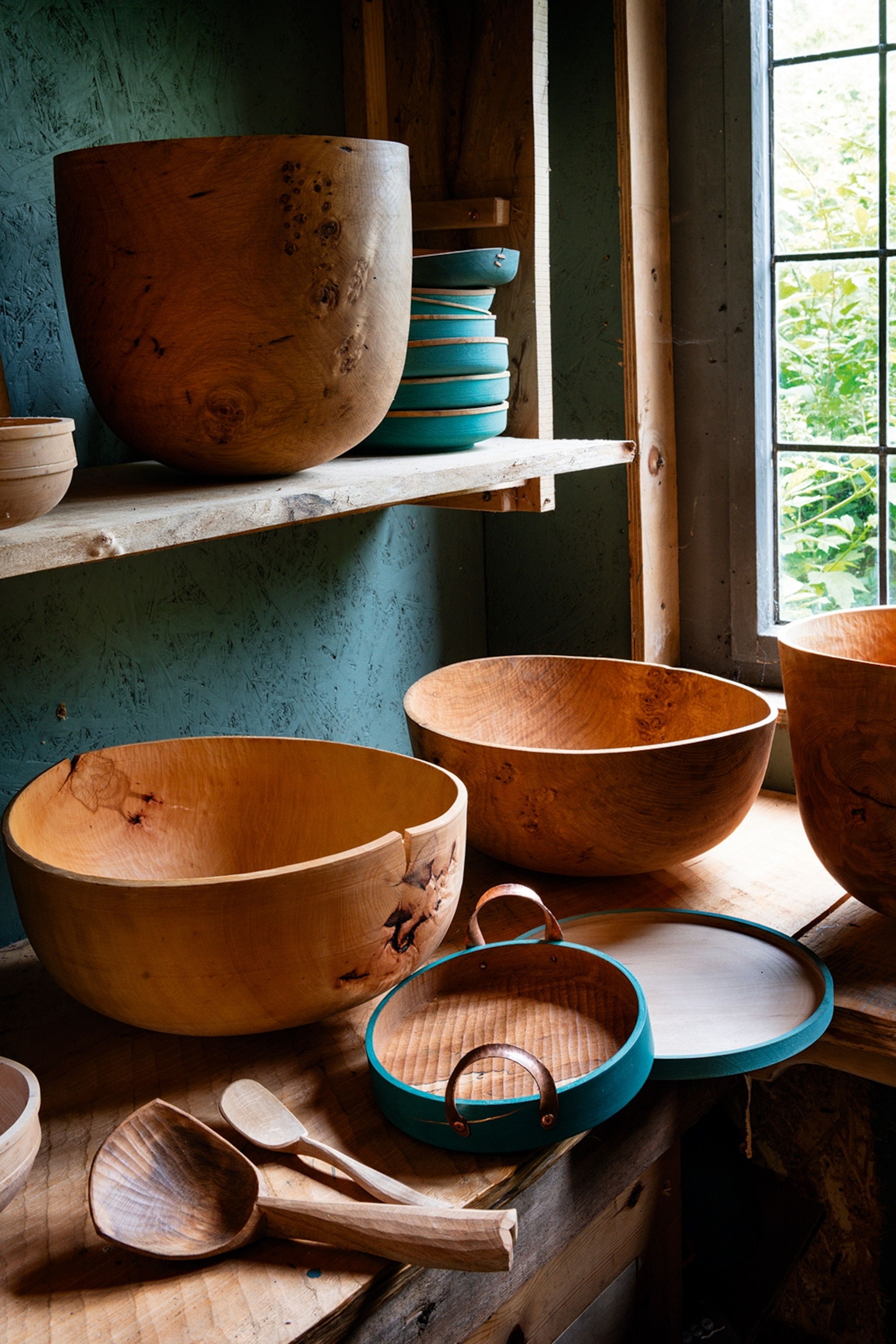 A close-up of smooth, wooden bowls on a shelf inside a simple studio hut.