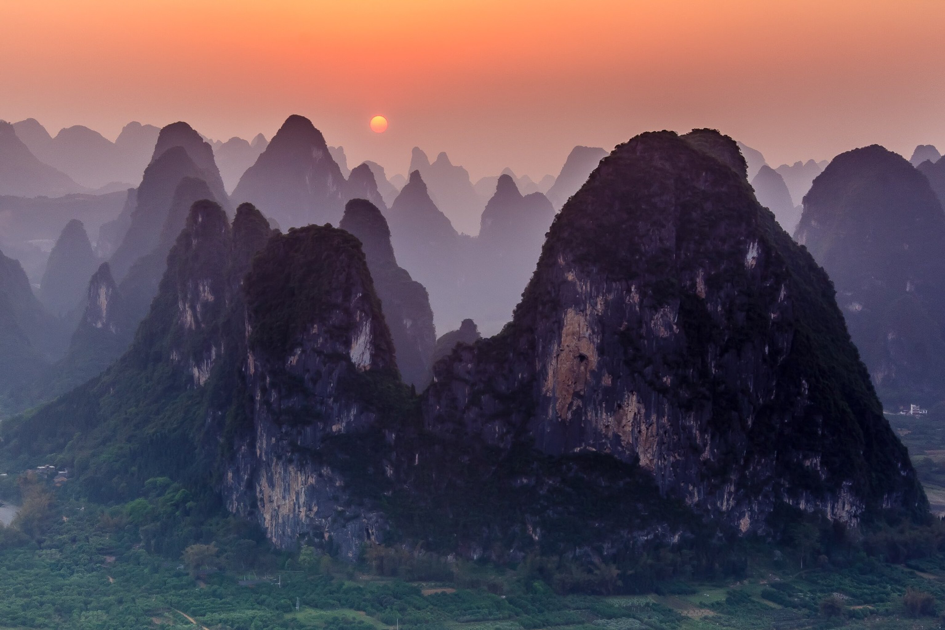 the sun setting over a mountain range in Xingping, China