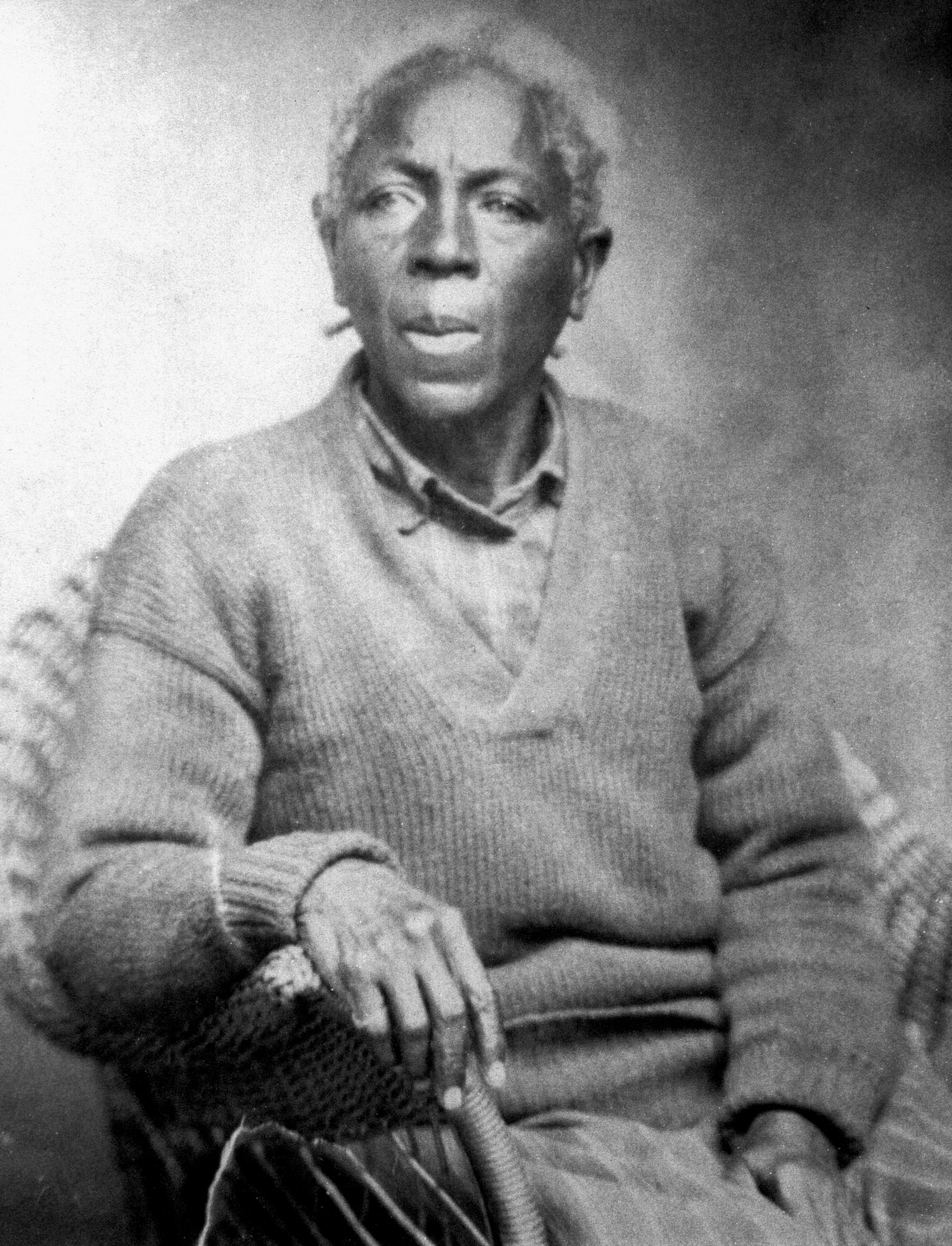 Black and white picture of a woman sitting, holding a cane