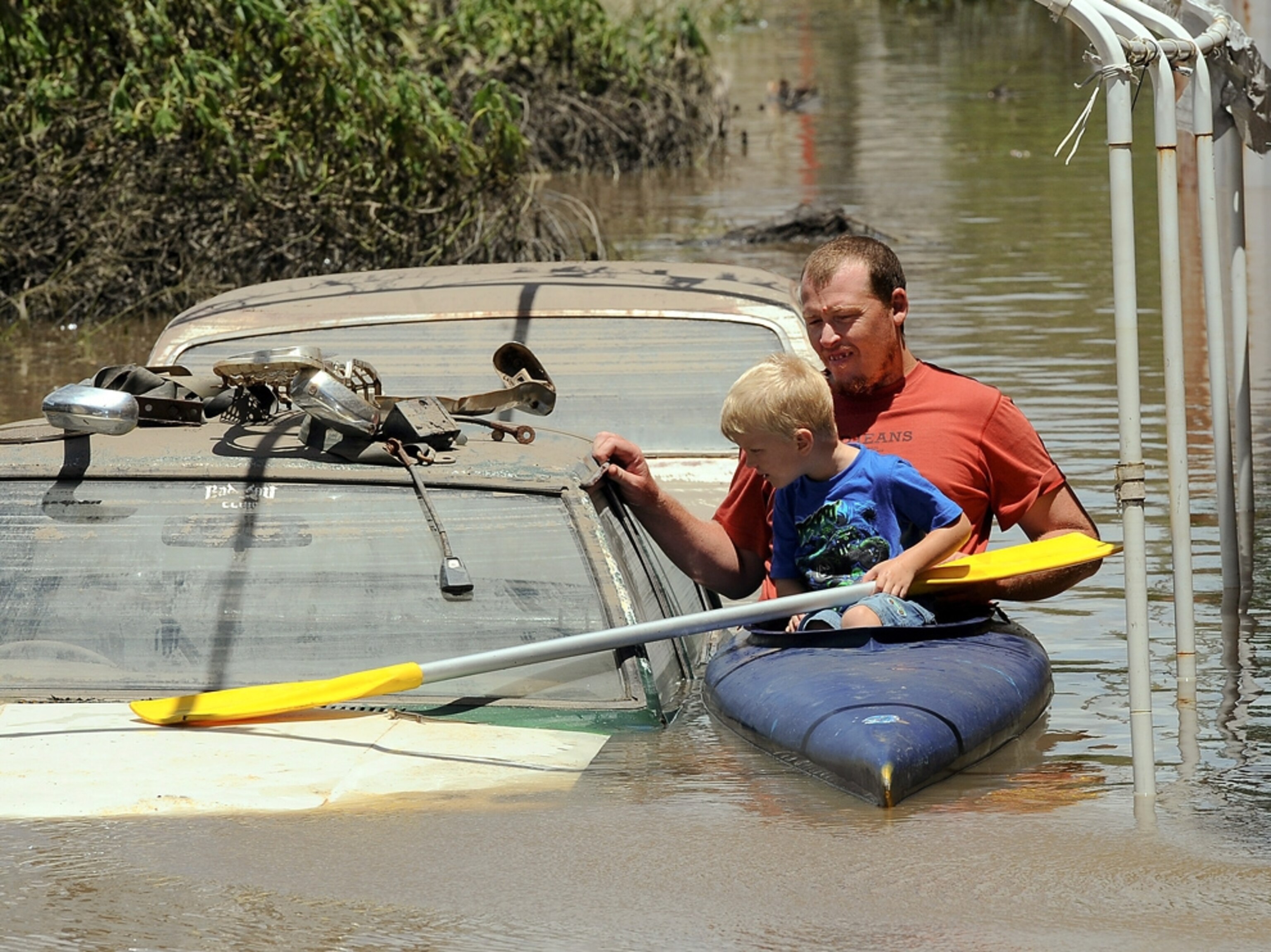 A man and a boy in kayak float past a submerged car