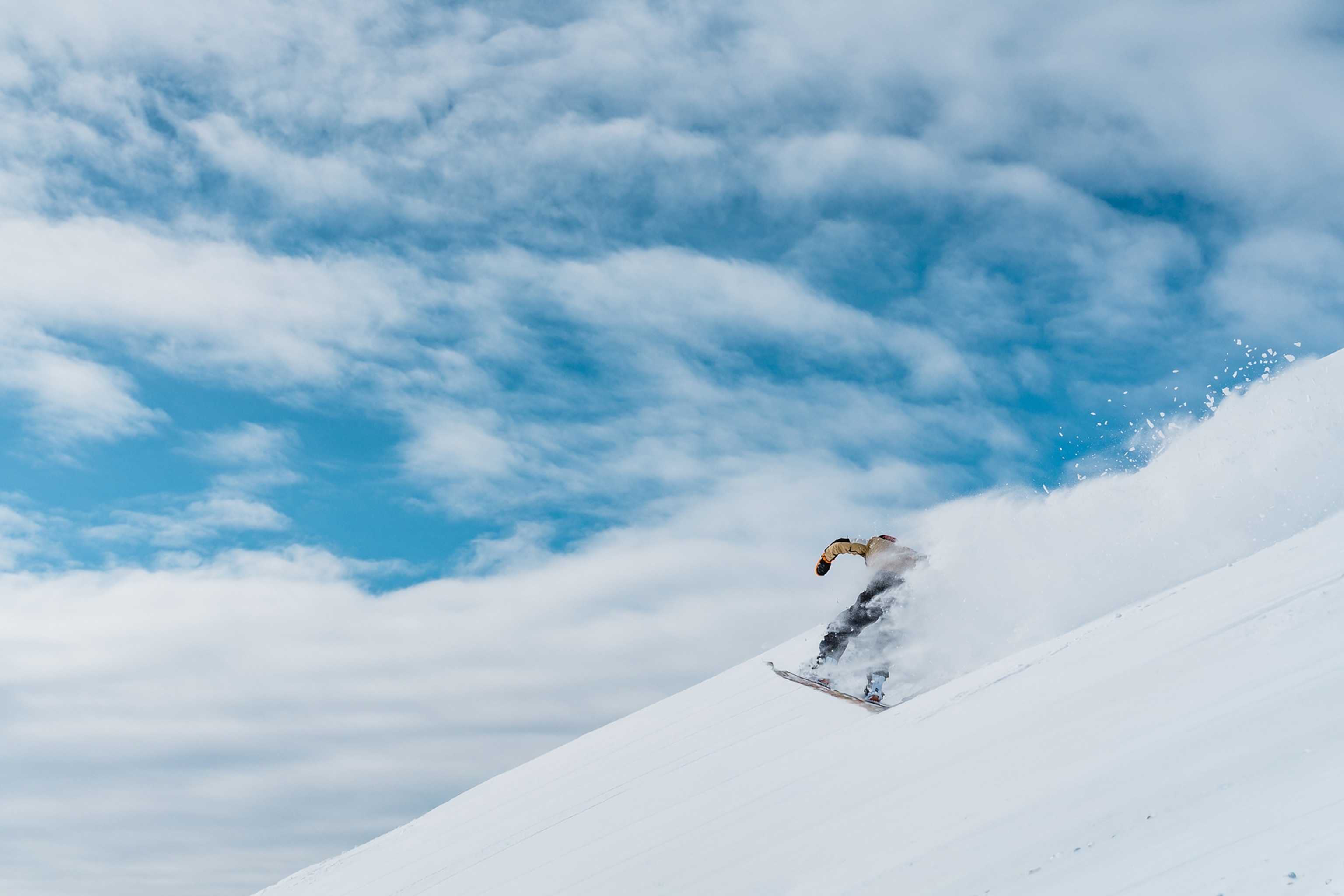 A snowboarder sliding down a slope with powder rising behind.
