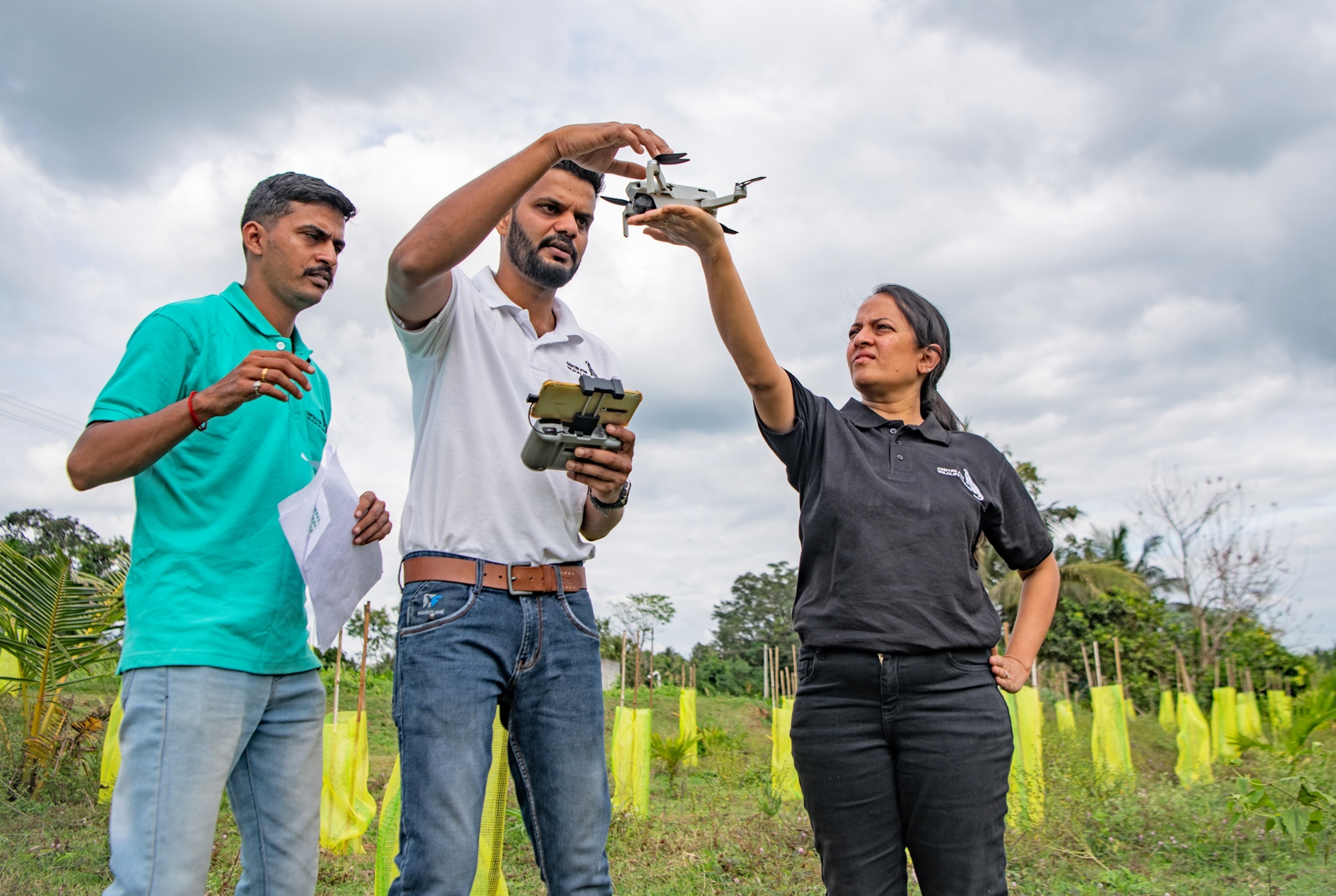 Women holds the drone on the palm of her raised hand and man adjusting it while another man is ready to help.