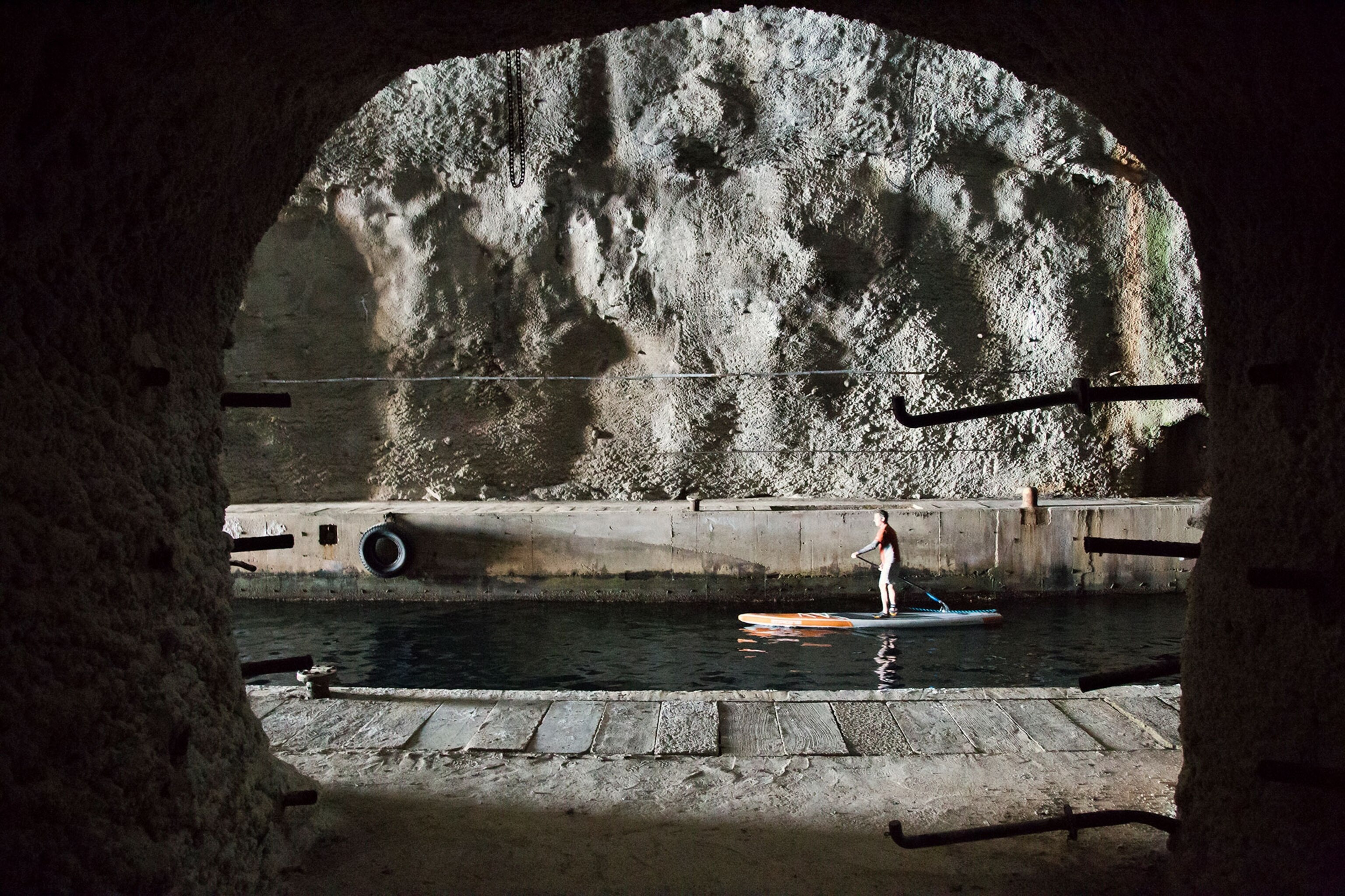 a stand-up paddle boarder paddling through a Cold War submarine cave in Croatia