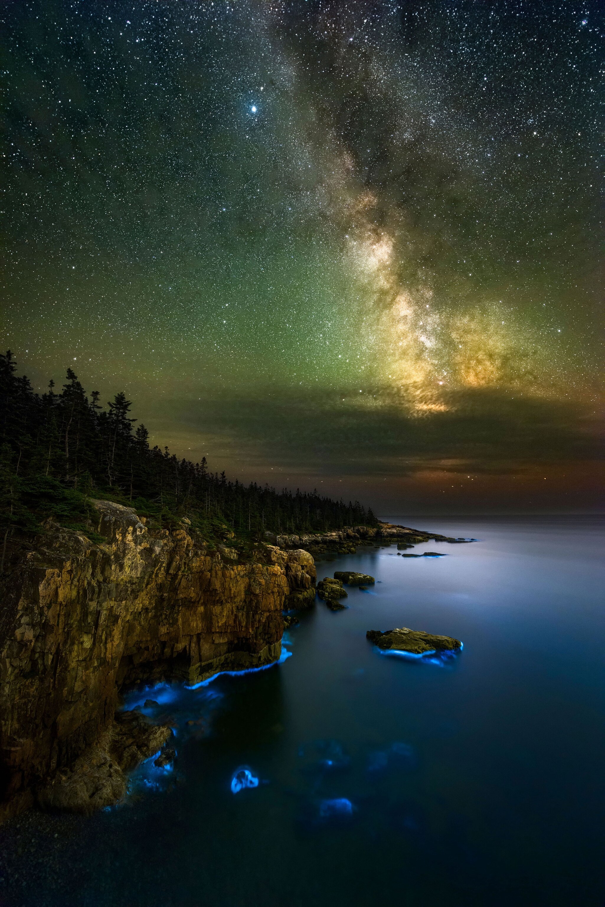 a bioluminescence in the water under the Milky Way along the rugged coast of Maine