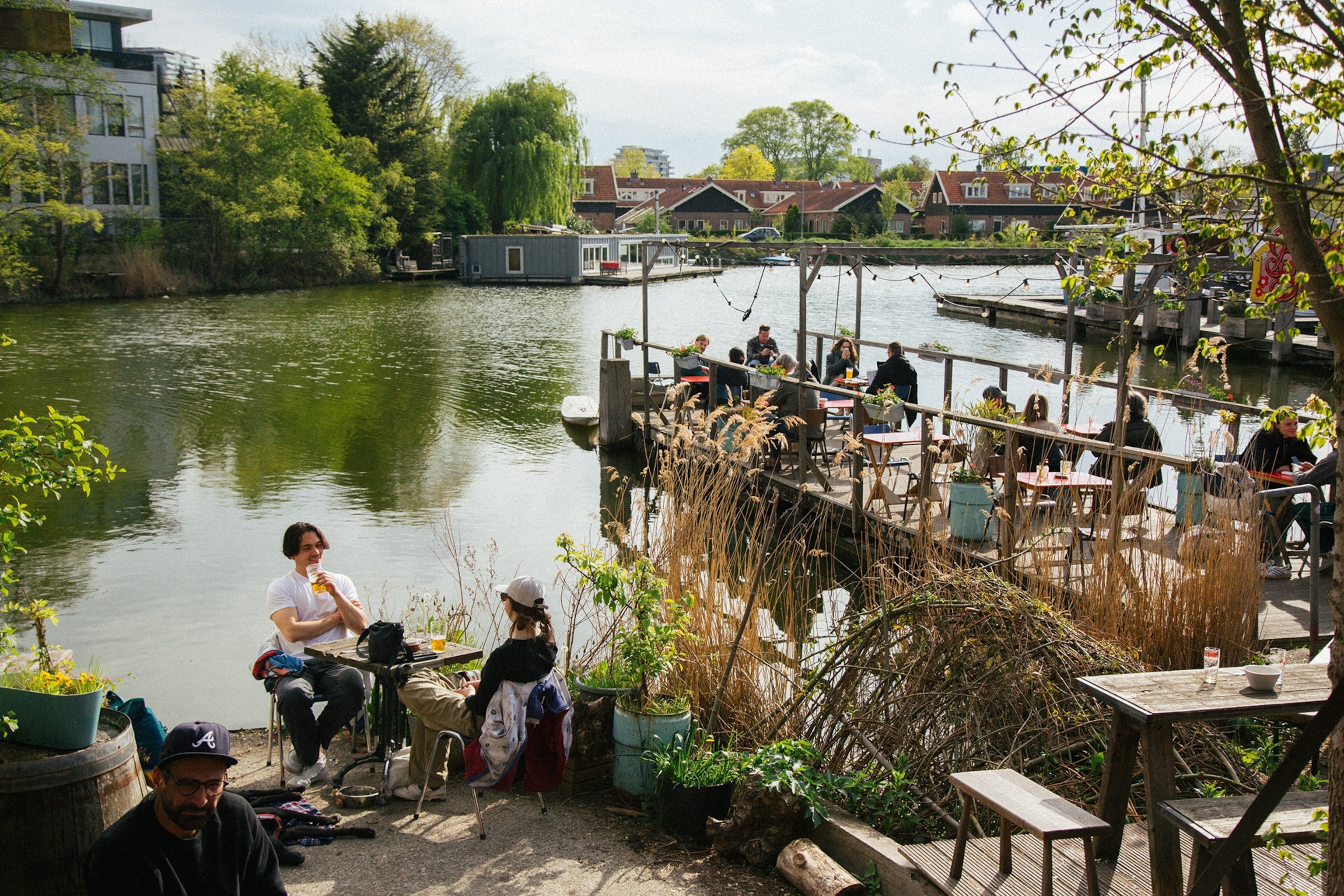 A wide-angled view onto a sunny canal-side cafe, where guests sit right by the water.