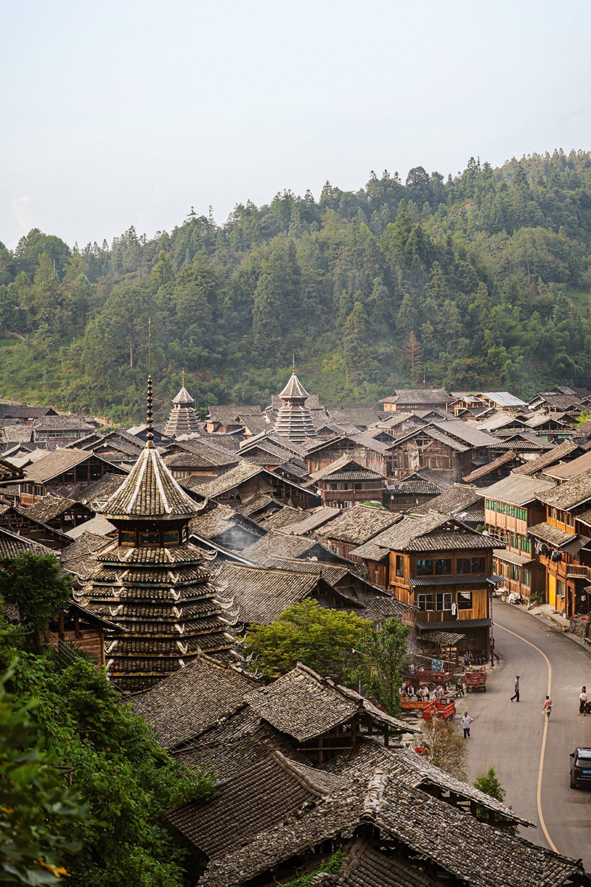A birds-eye perspective onto a small mountain village with wooden towers peeking through the otherwise low-rising wooden houses.