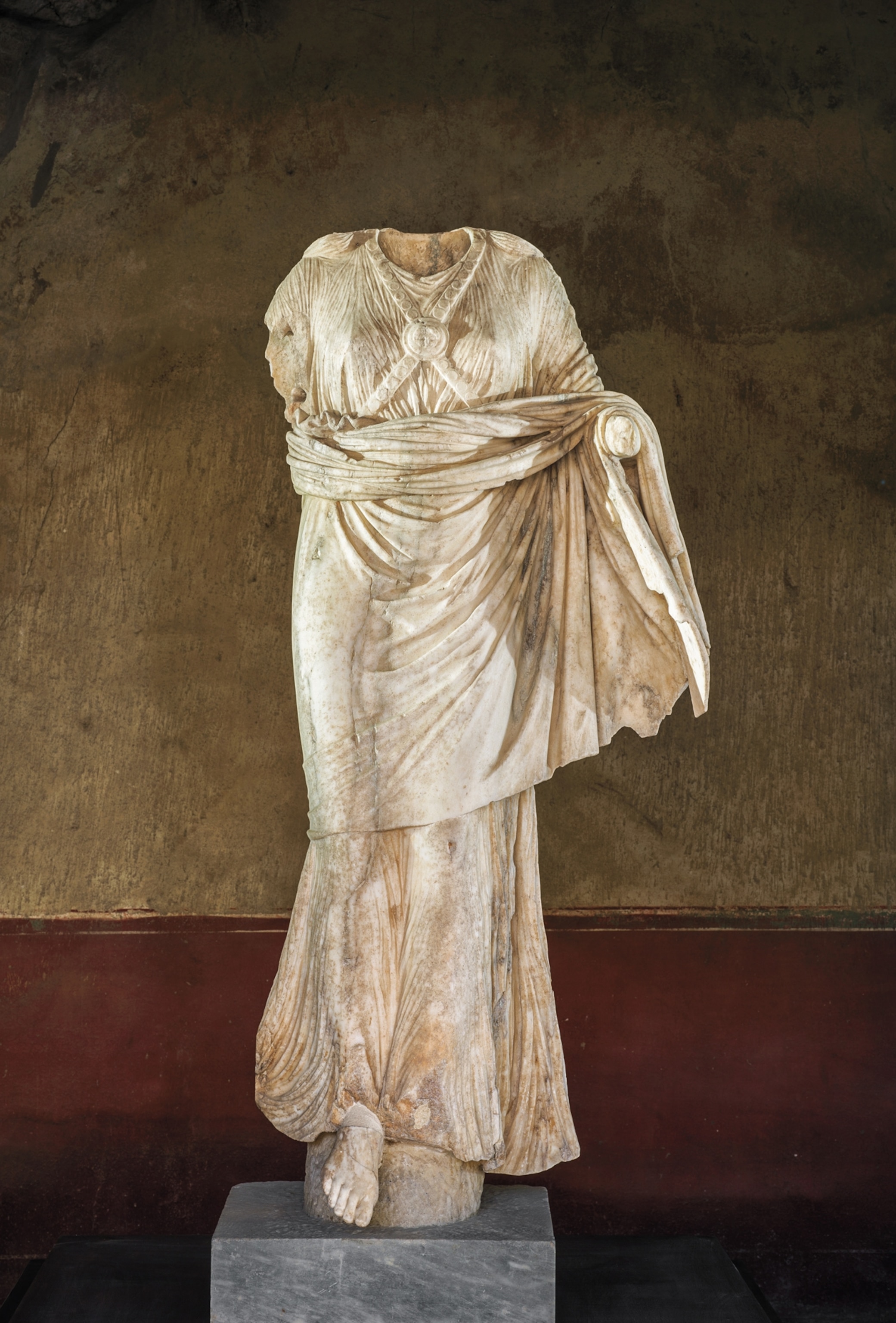 A headless statue stands in front of a wall
