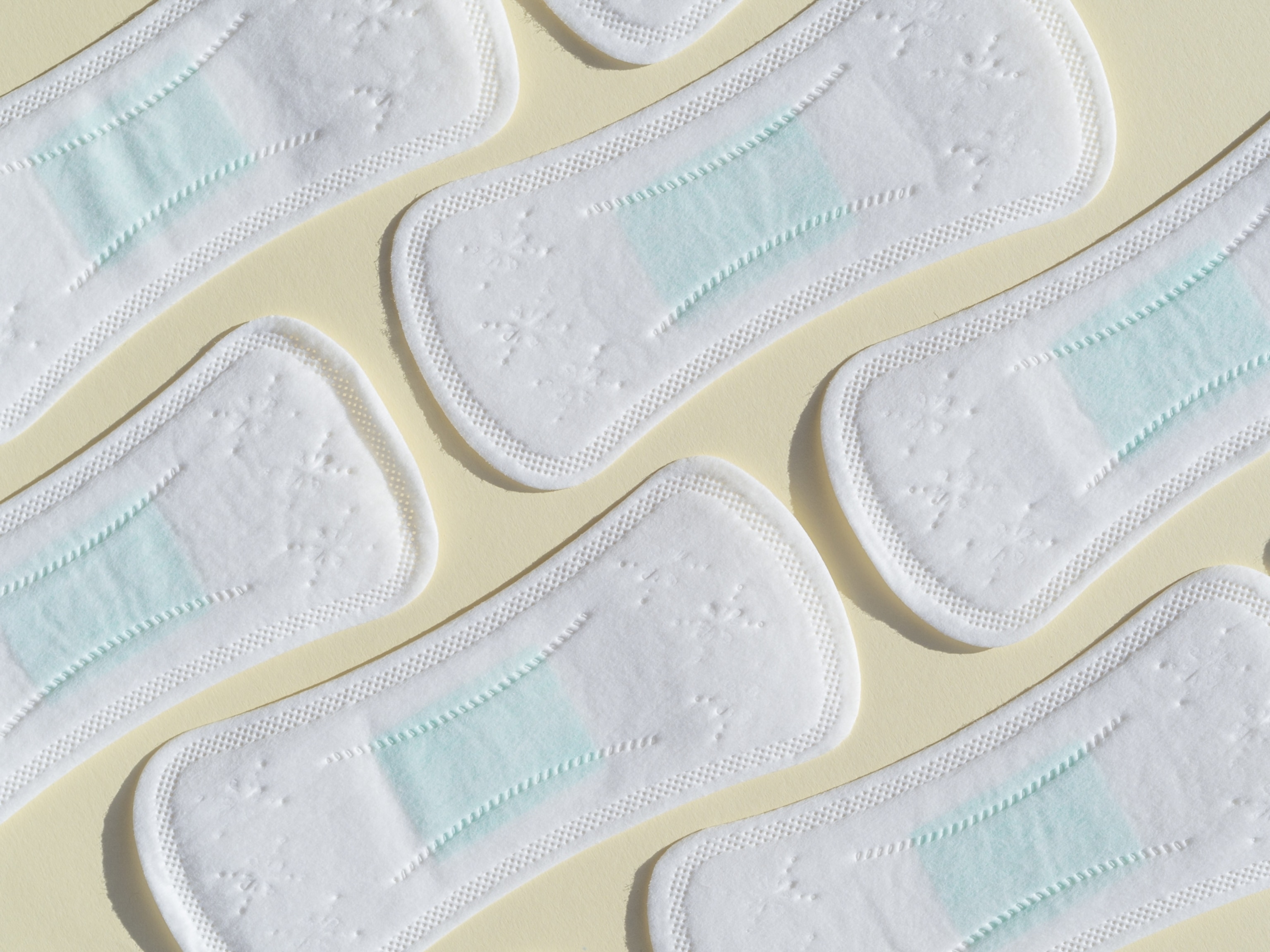 A pattern of white sanitary pads with light blue accents arranged diagonally on a beige background,