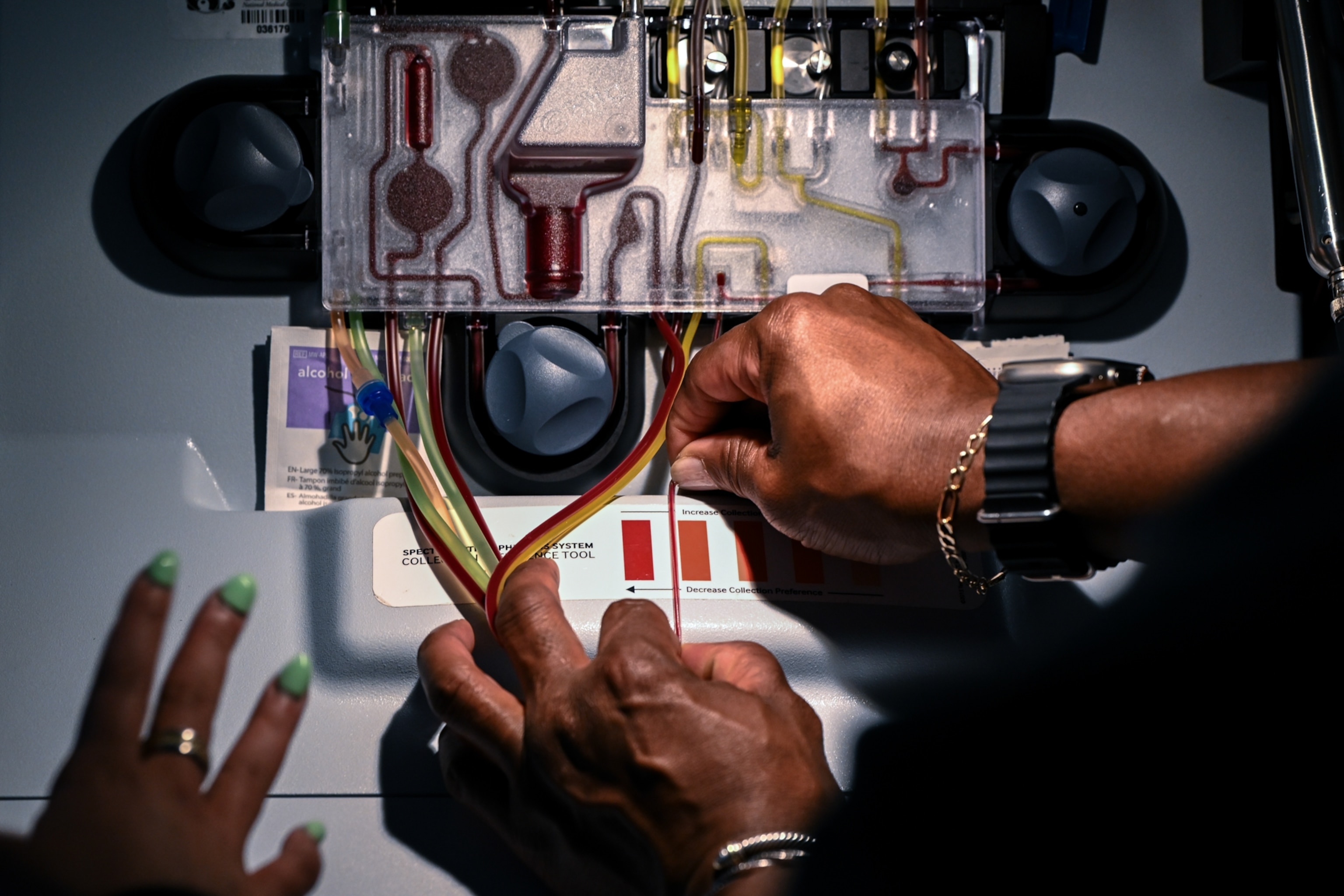 Close-up of hands operating a medical machine, adjusting red and yellow tubes.