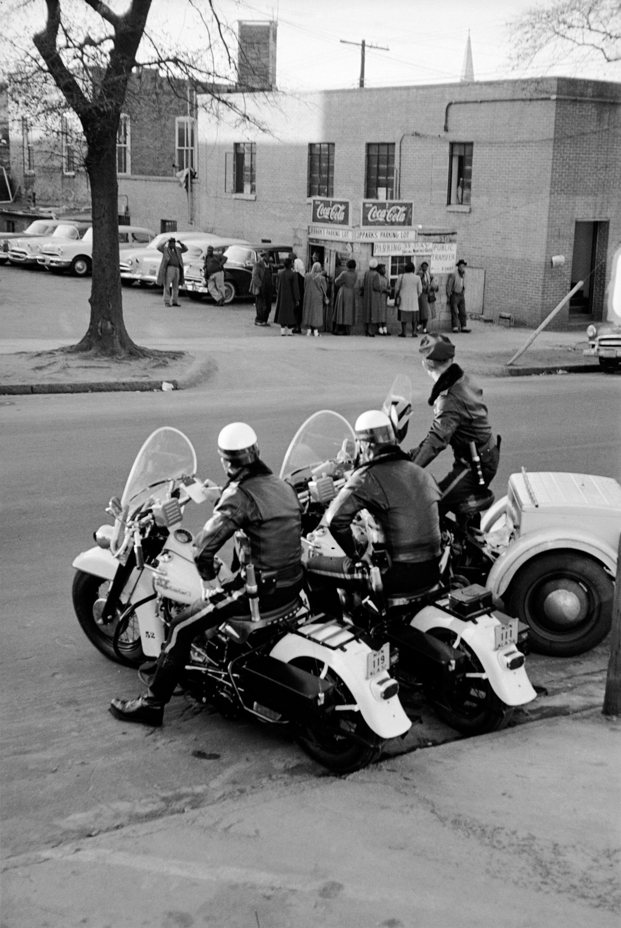 Police officers sitting on motorcycles as they watch a crowd of African Americans lining up for a carpool