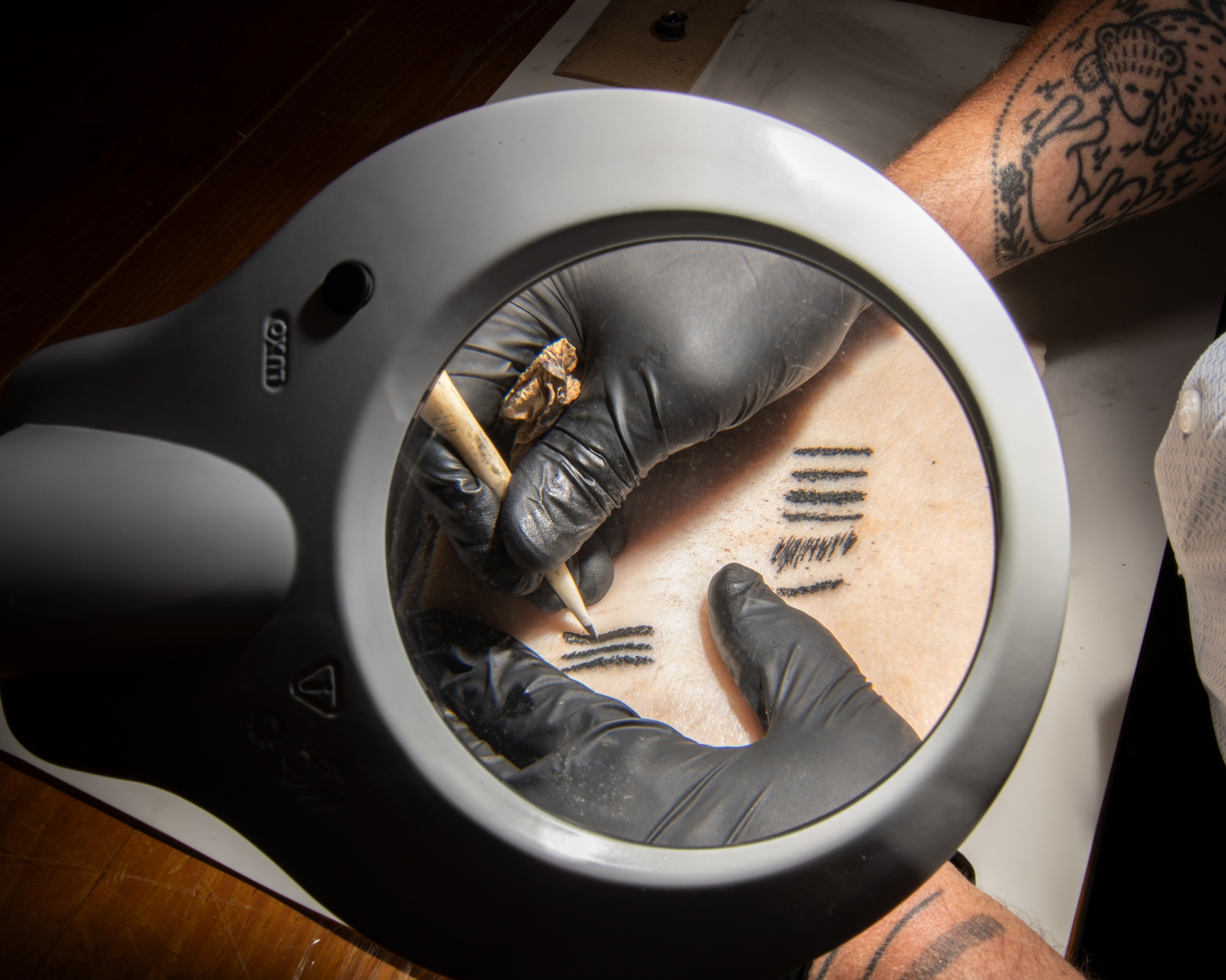Hand in gloves drawing lines under round magnify glass.