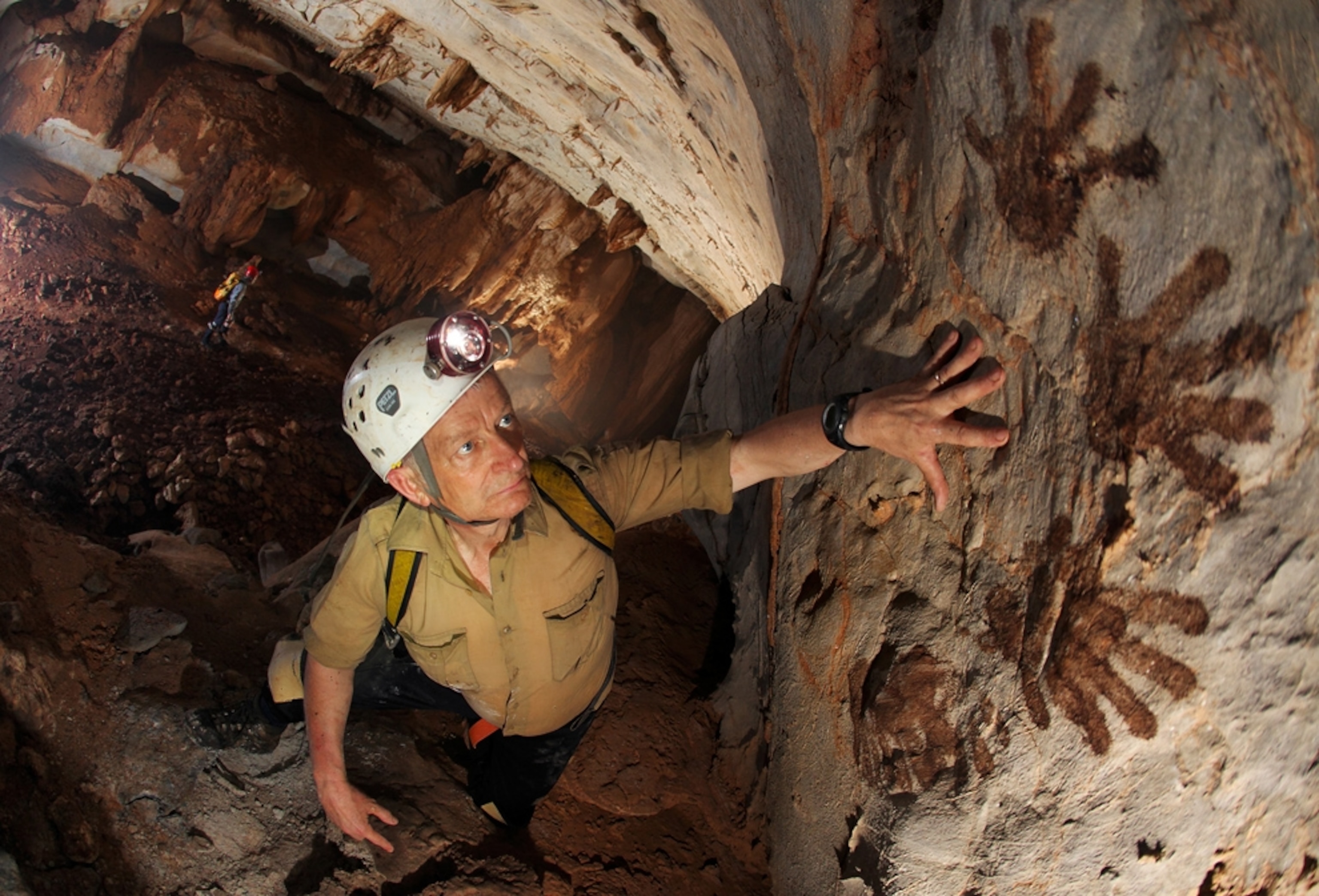 a man comparing his hand to painted prints in a Borneo cave.