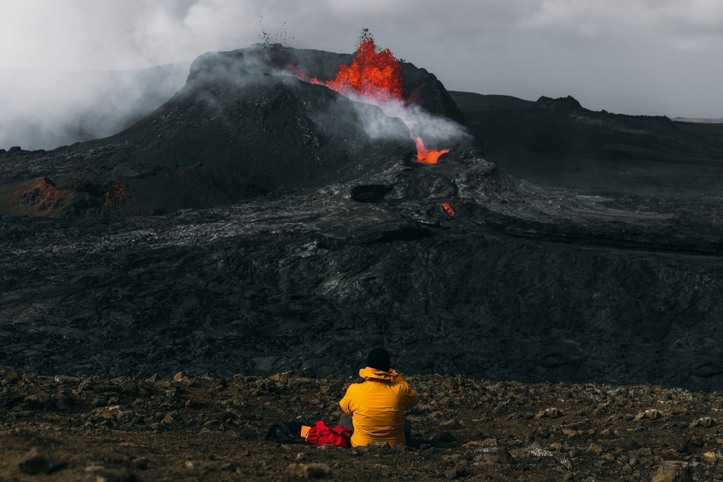 A photographer perches on the edge of a volcano and shoots an eruption from a safe distance.