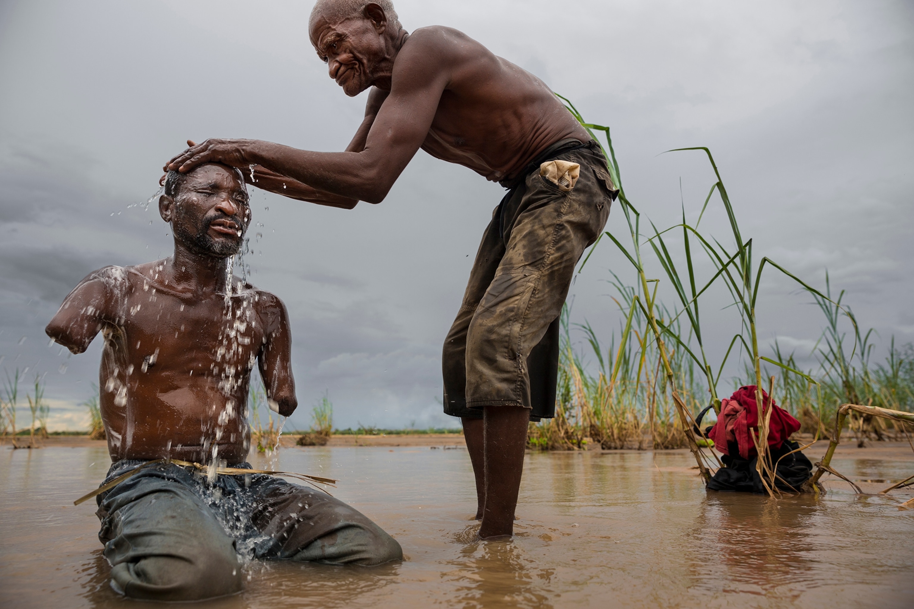 Yusufu Shabani Difika lost his arms in a lion attack in Tanzania’s Selous Game Reserve. Poor villagers farm marginal land along reserve edges, where bushpigs raid crops and lions may attack people. Here his uncle bathes Difika, a father of two.