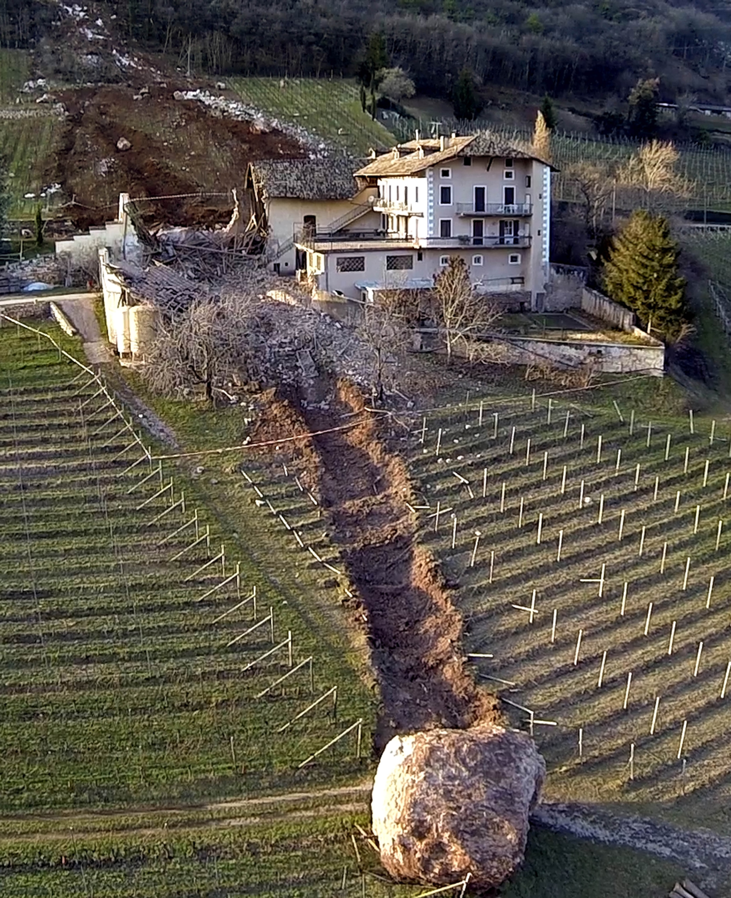 In this photo provided by Tareom.com Thursday, Jan. 30, 2014, and taken on Jan. 23, 2014, a huge boulder is seen after it missed a farm house by less than a meter, destroying the barn, and stopped in the vineyard, while a second giant boulder, which detached during the same landslide on Jan. 21, 2014, stopped next to the house, in Ronchi di Termeno, in Northern Italy.