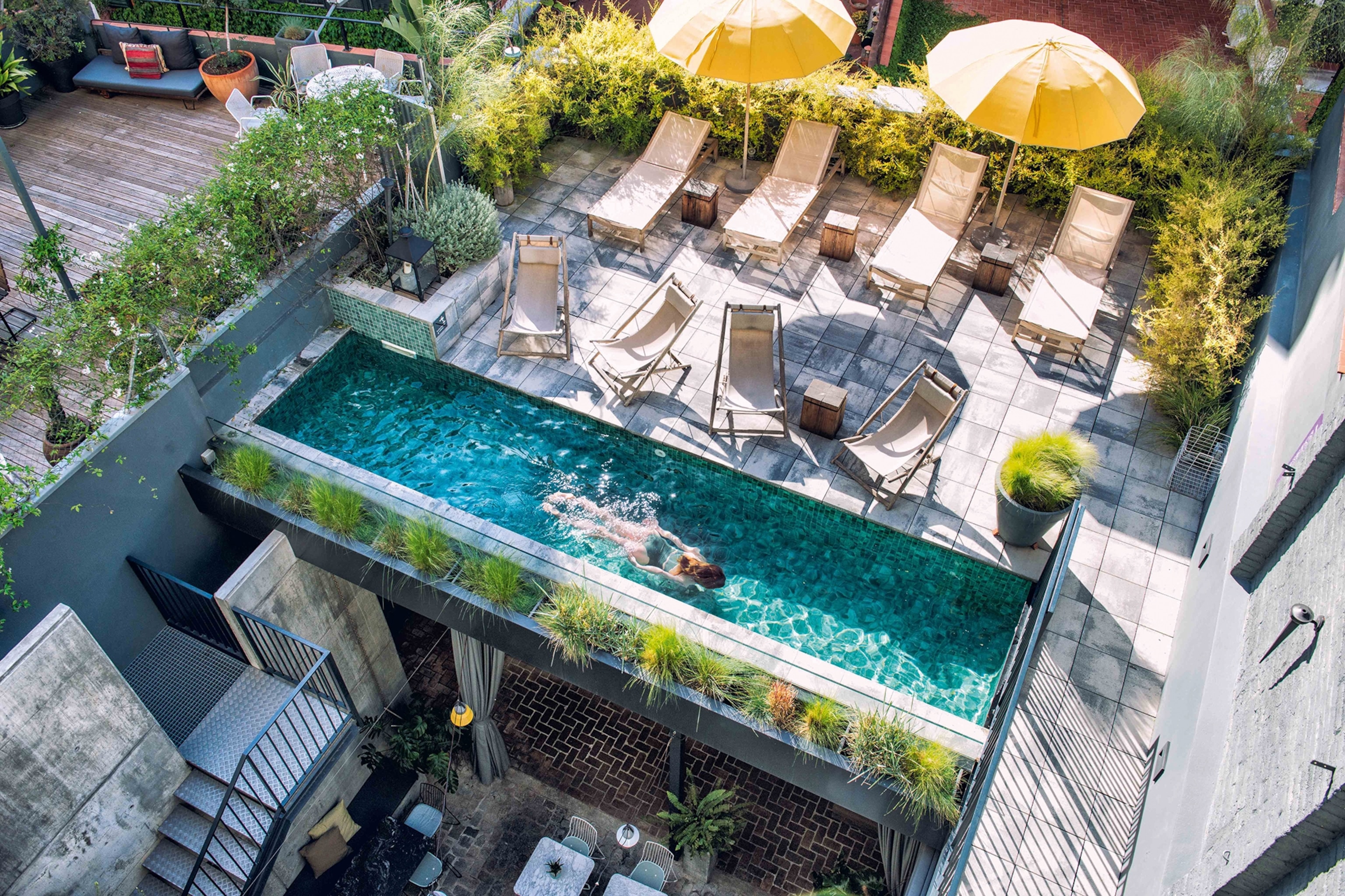 A birds-eye view onto a rooftop pool with sun chairs and an adjoining terrace.