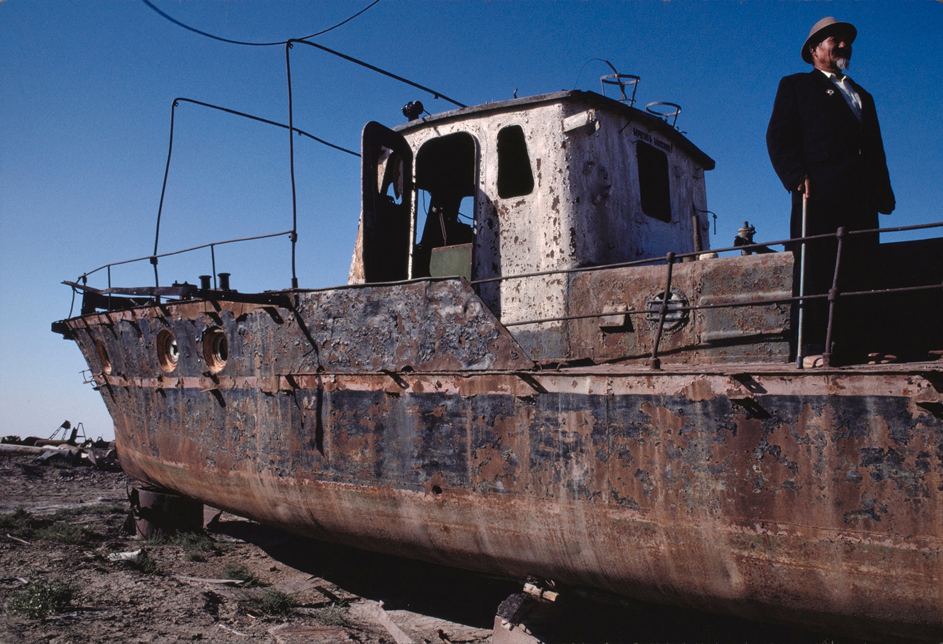 A man looks out from a rusty boat he once captained.