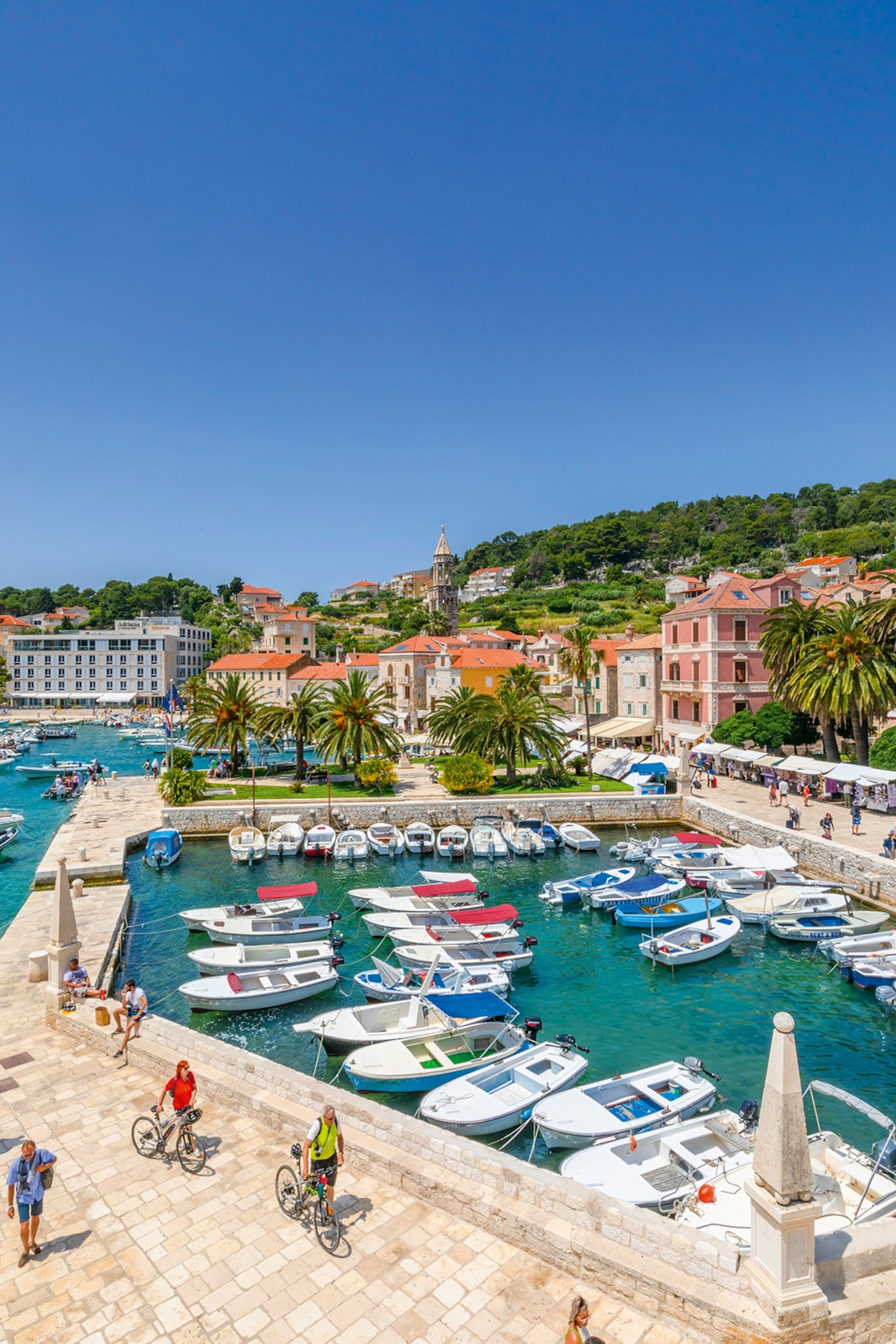 An enclosed harbour bay with low stone walls, turning the outer walkway into a bridge, as small boats are anchored inside.
