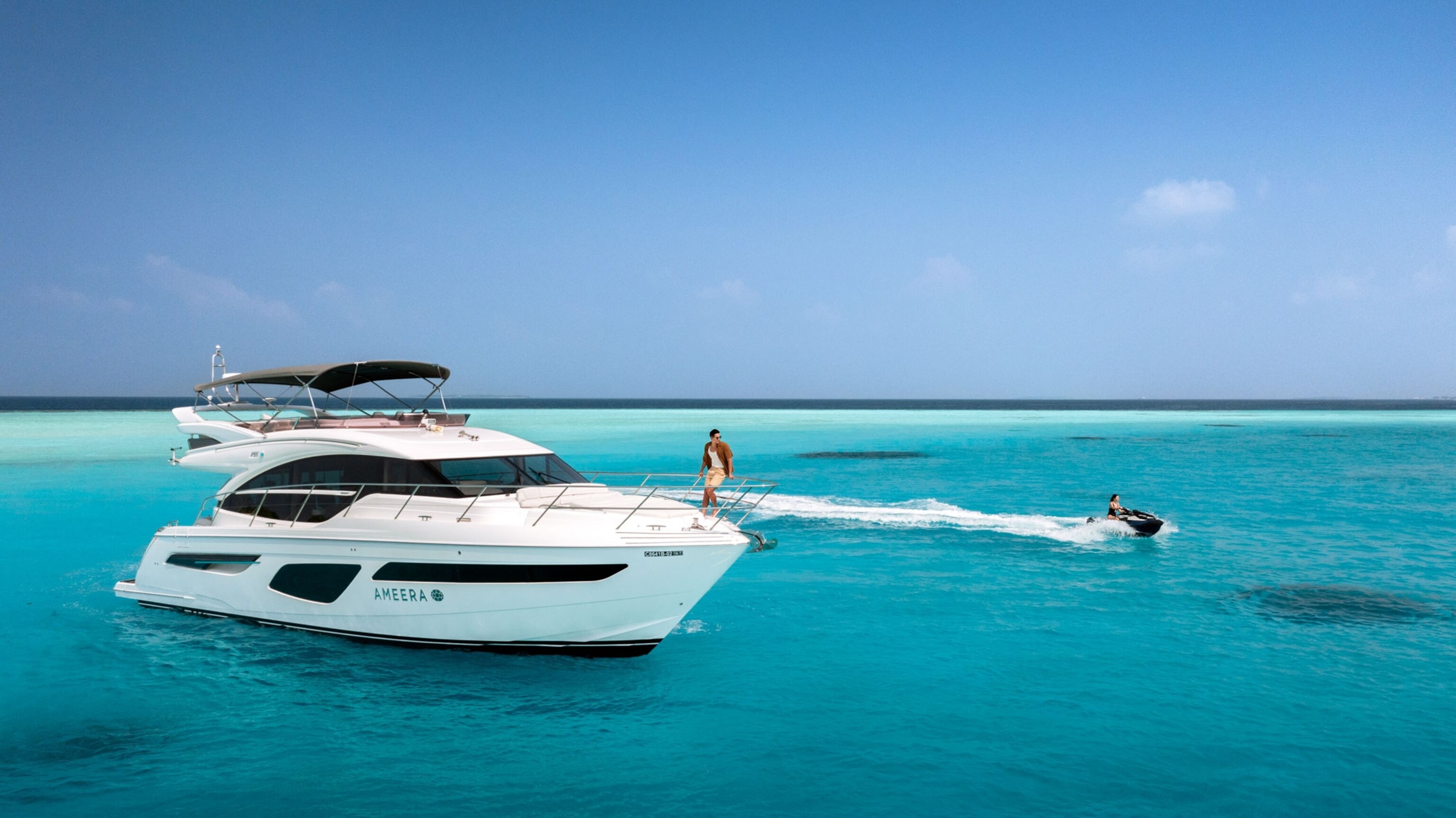 A yacht and a woman on a jet ski are seen side by side cruising through a turquoise ocean.