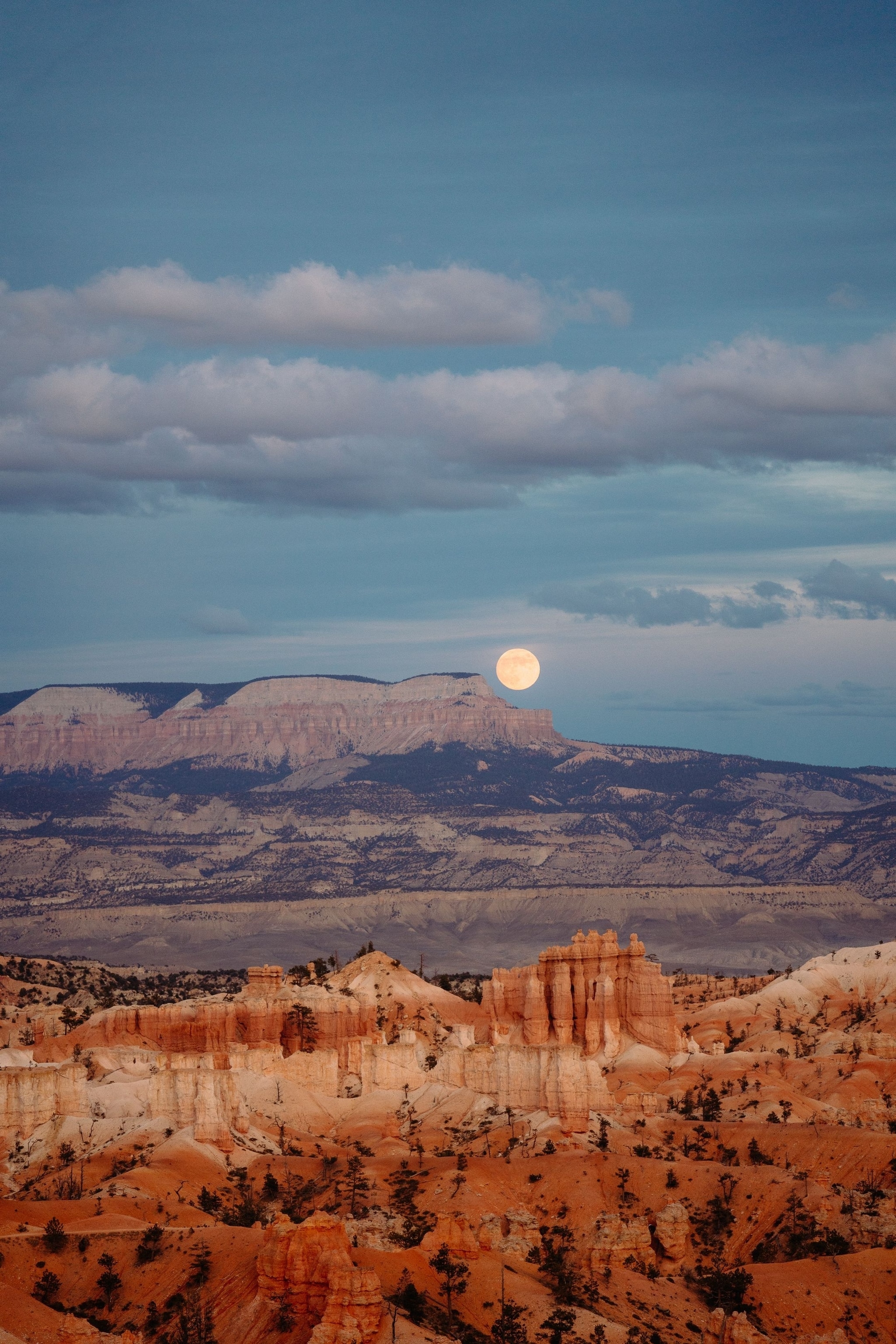 The full moon is visible over orange mountains